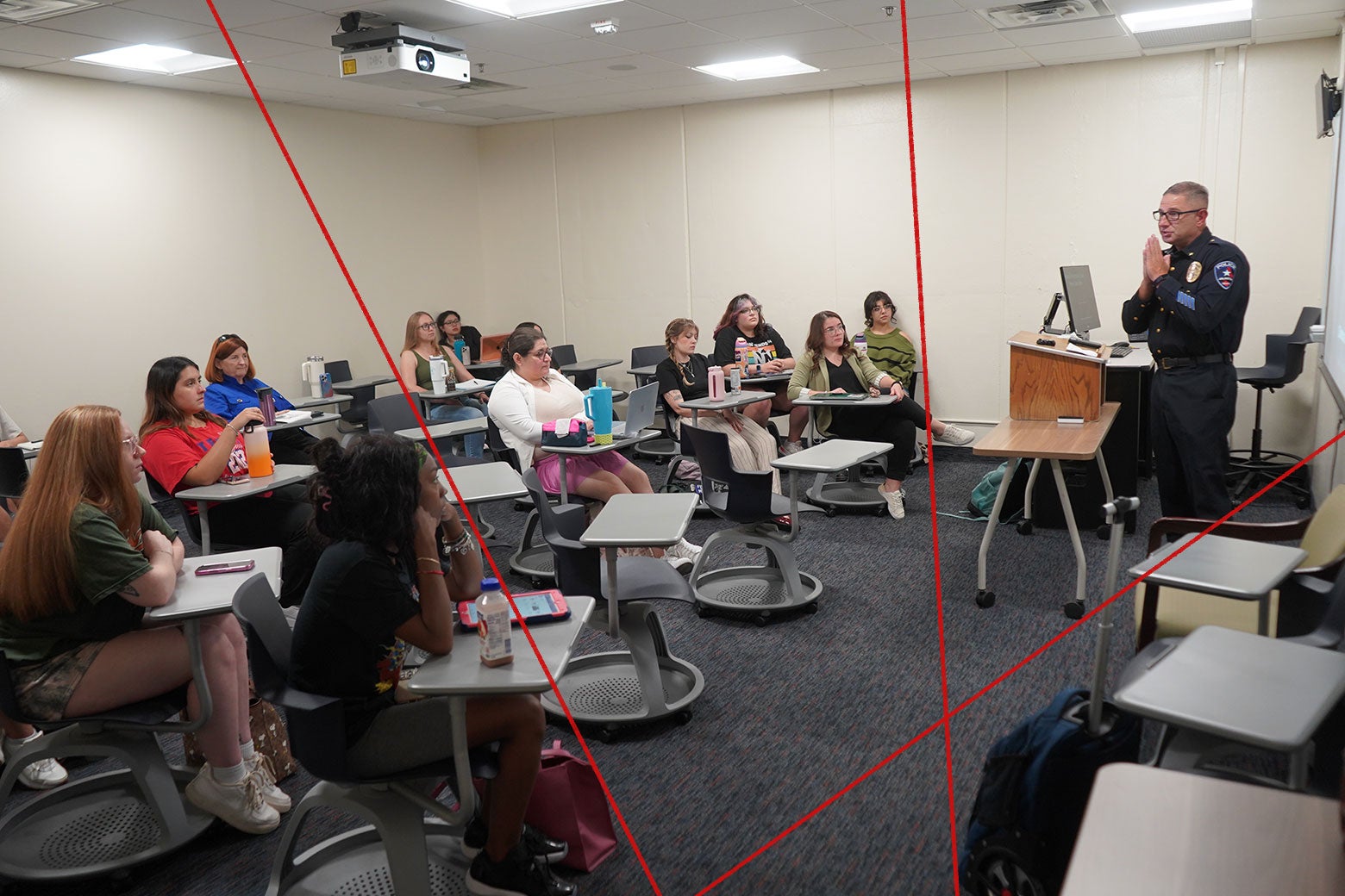 A police officer standing behind a lectern, addressing a roomful of college students.