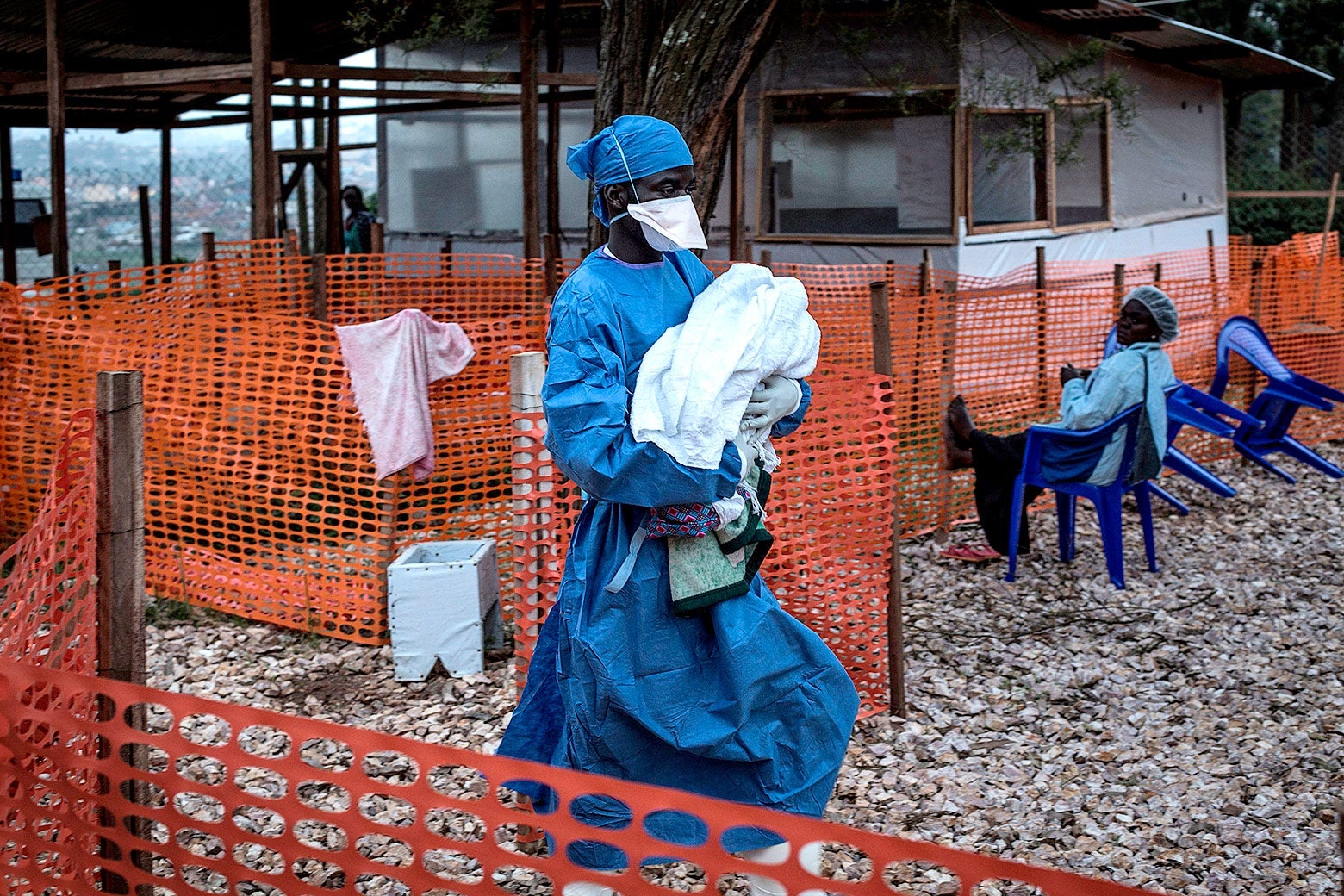 A health worker carries a baby behind orange fencing.