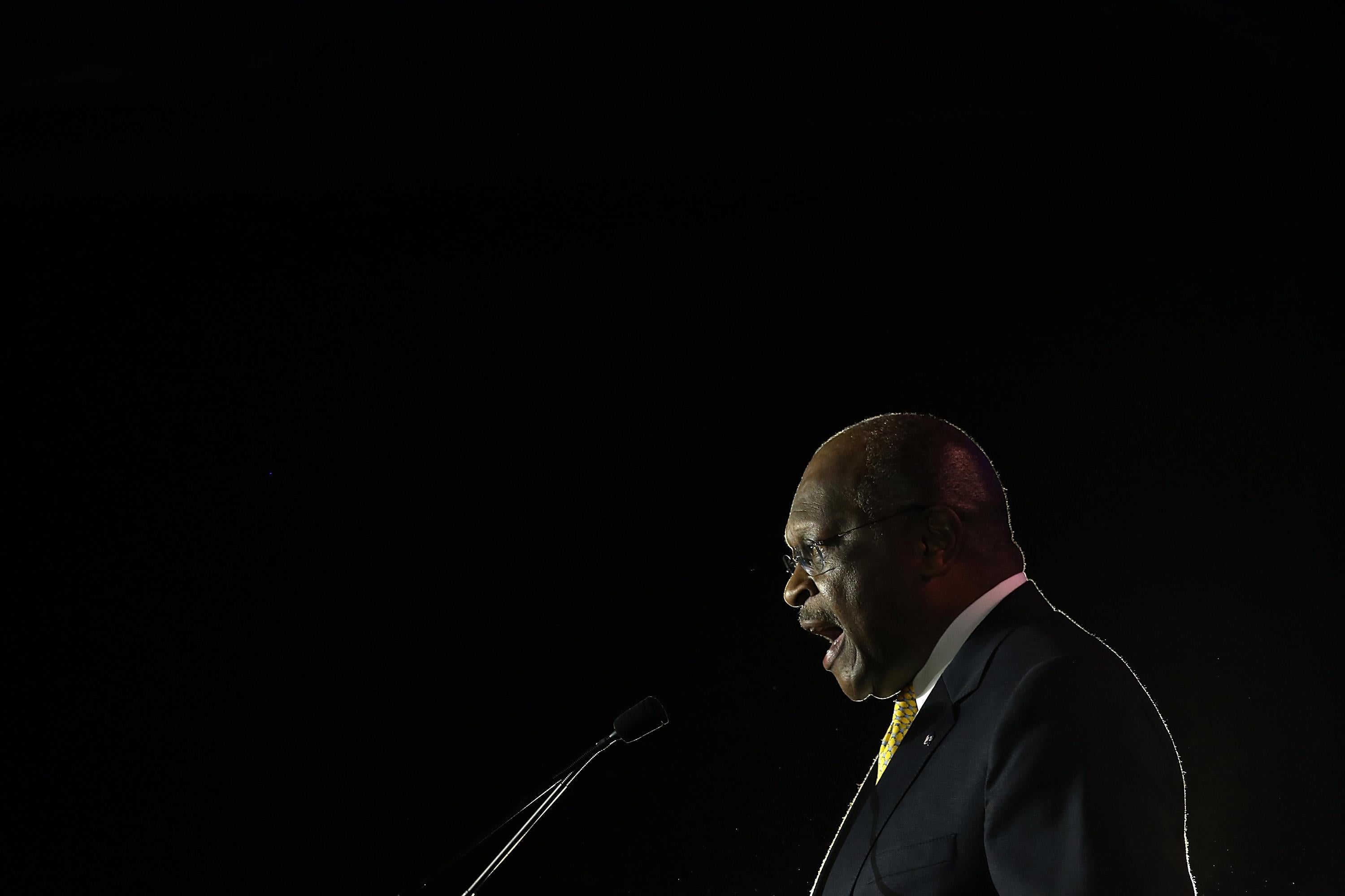 Herman Cain, in profile, speaking at a podium.