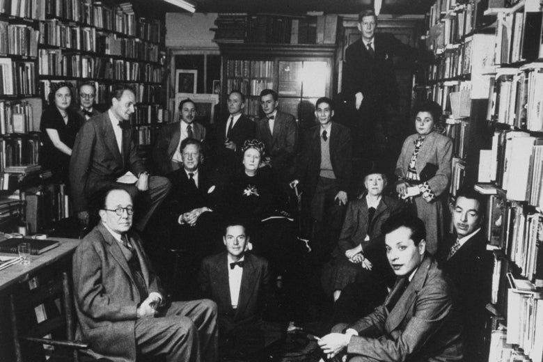 In black and white, the poets squeeze into a small room surrounded by books on shelves.