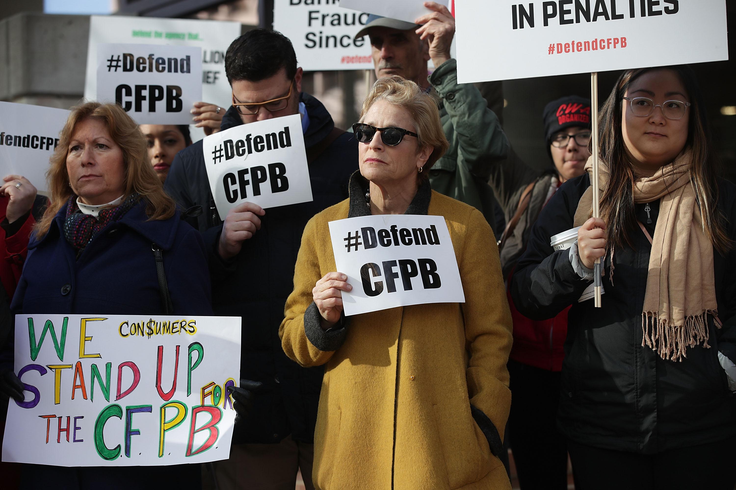 A crowd of protesters holding up signs defending the CFPB