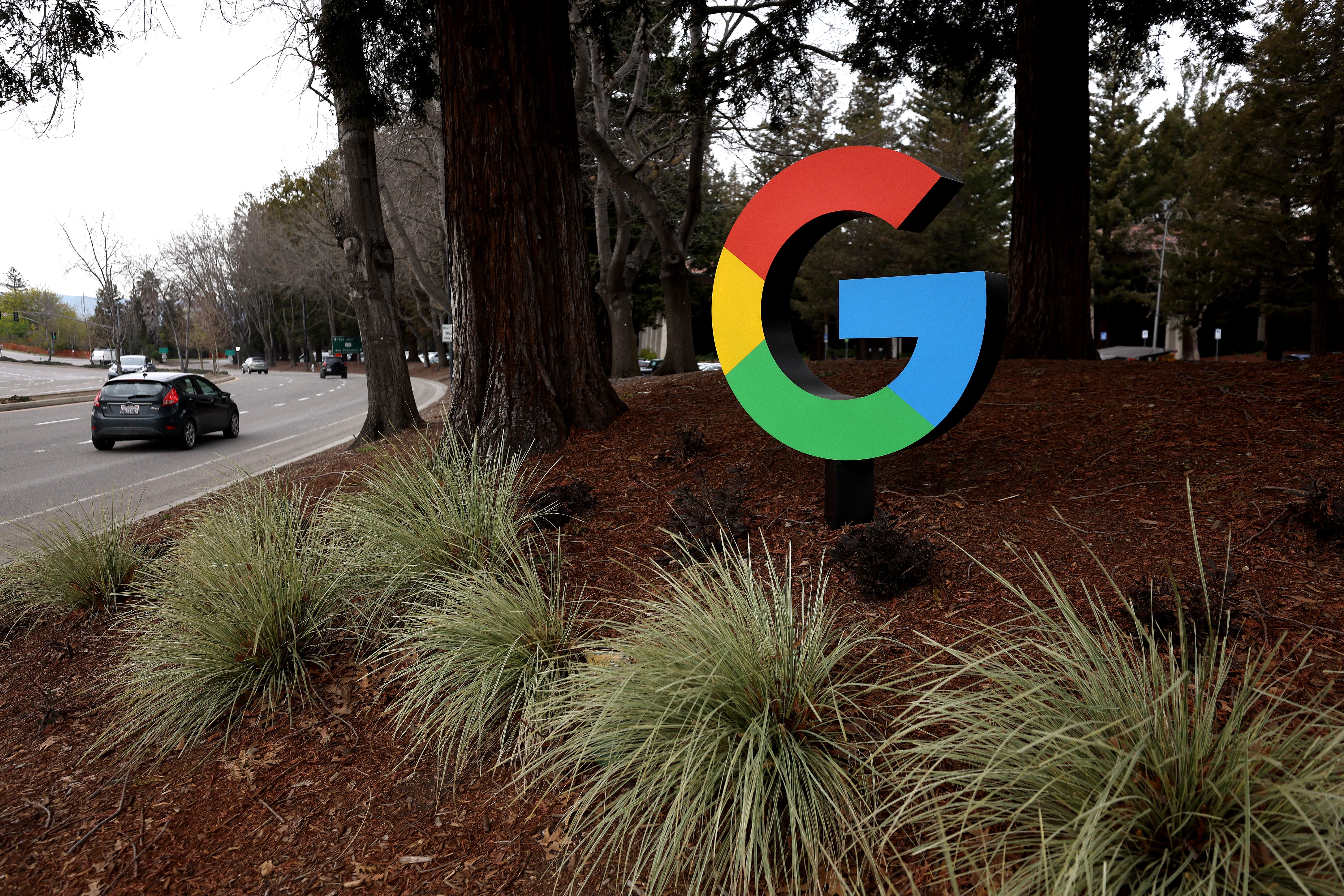 A sign for the Google logo stands amid a field of trees and grass.