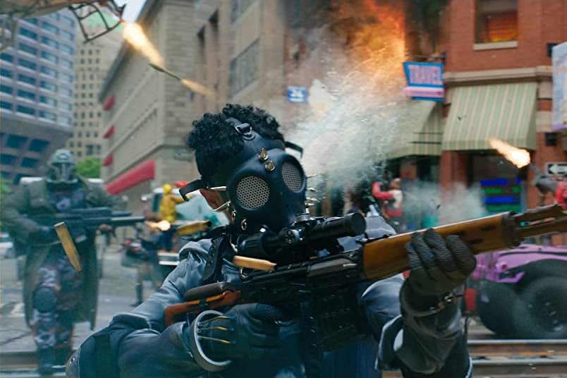 Ryan Reynolds, wearing a blue shirt, looks with confusion at a man in a gas mask firing a rifle.