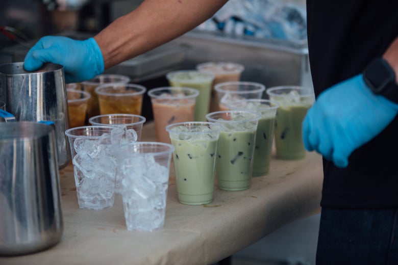 A person wearing blue latex gloves prepares several cups of iced milk tea.