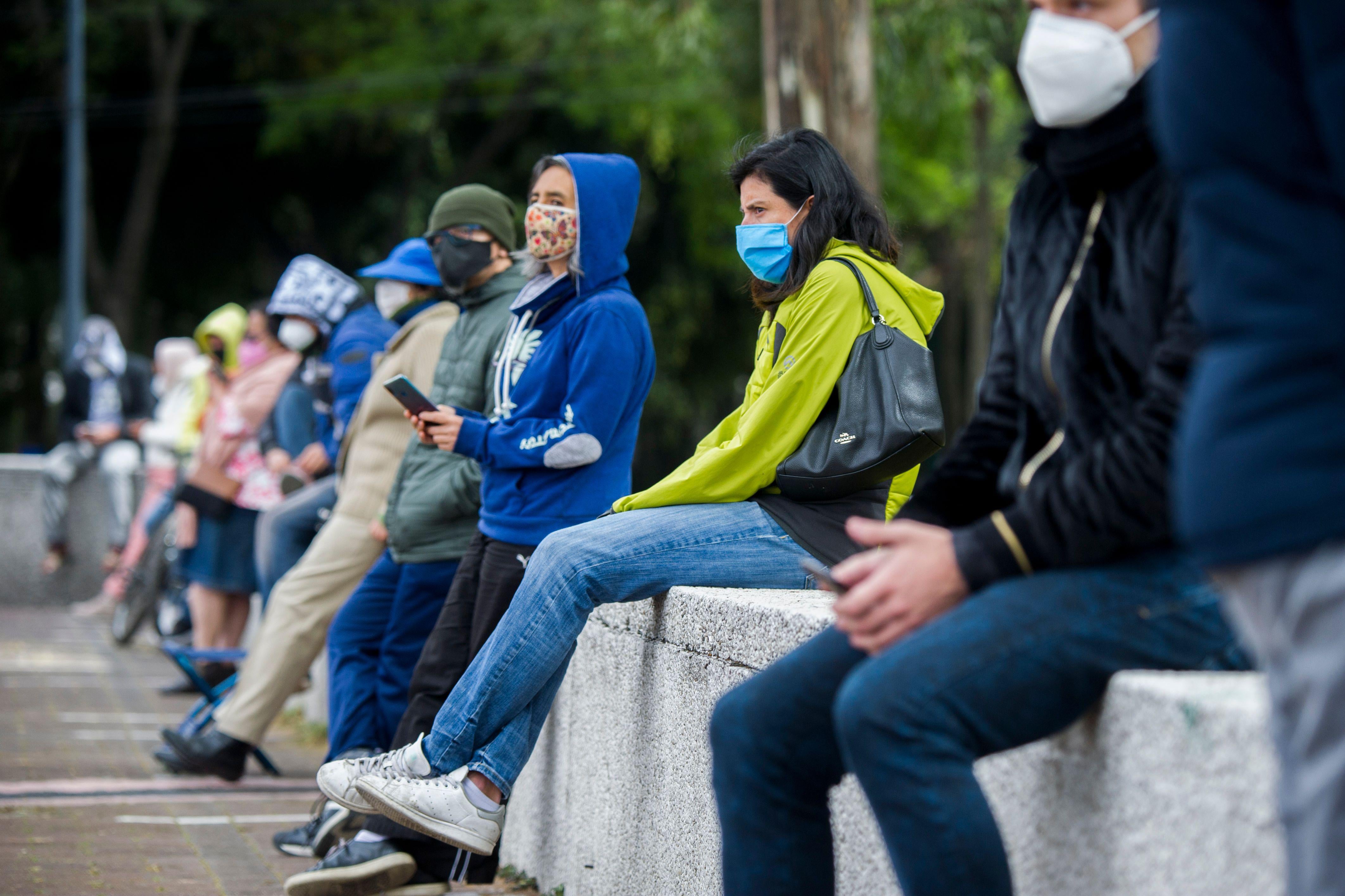 People wearing masks sit on a low wall.
