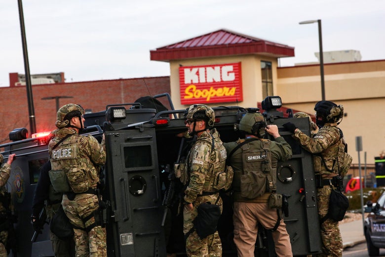 Law enforcement officers in camo tactical gear stand on an armored vehicle in the parking lot