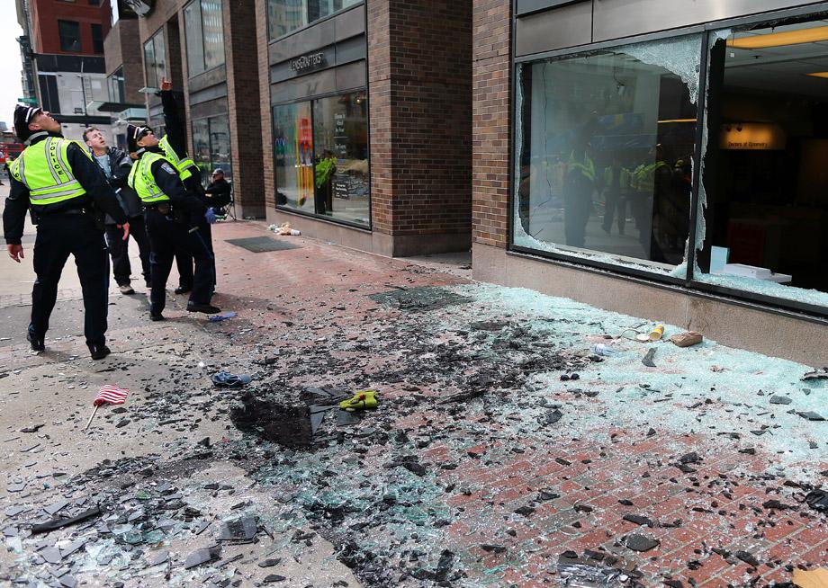 Boston Police look at blown out windows at the scene of the first explosion on Boylston Street near the finish line of the Boston Marathon.