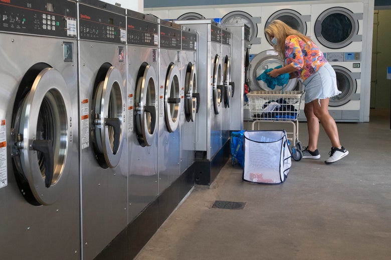 A woman wearing a face mask does her laundry in a laundromat.