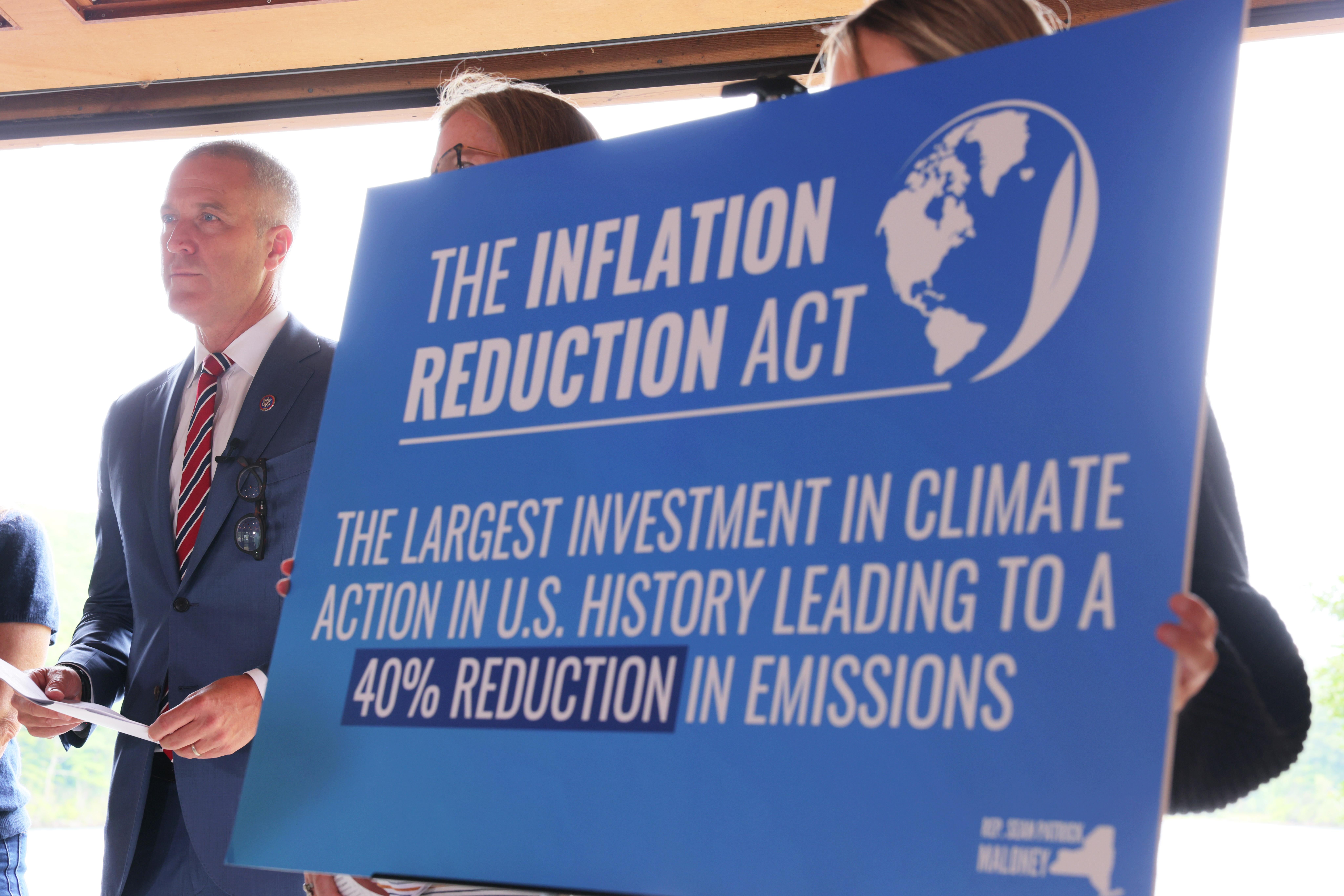 Rep. Sean Patrick Maloney stands in a suit behind a blue sign that says "The Inflation Reduction Act: the largest investment in climate action in U.S. history leading to a 40 percent reduction in emissions."