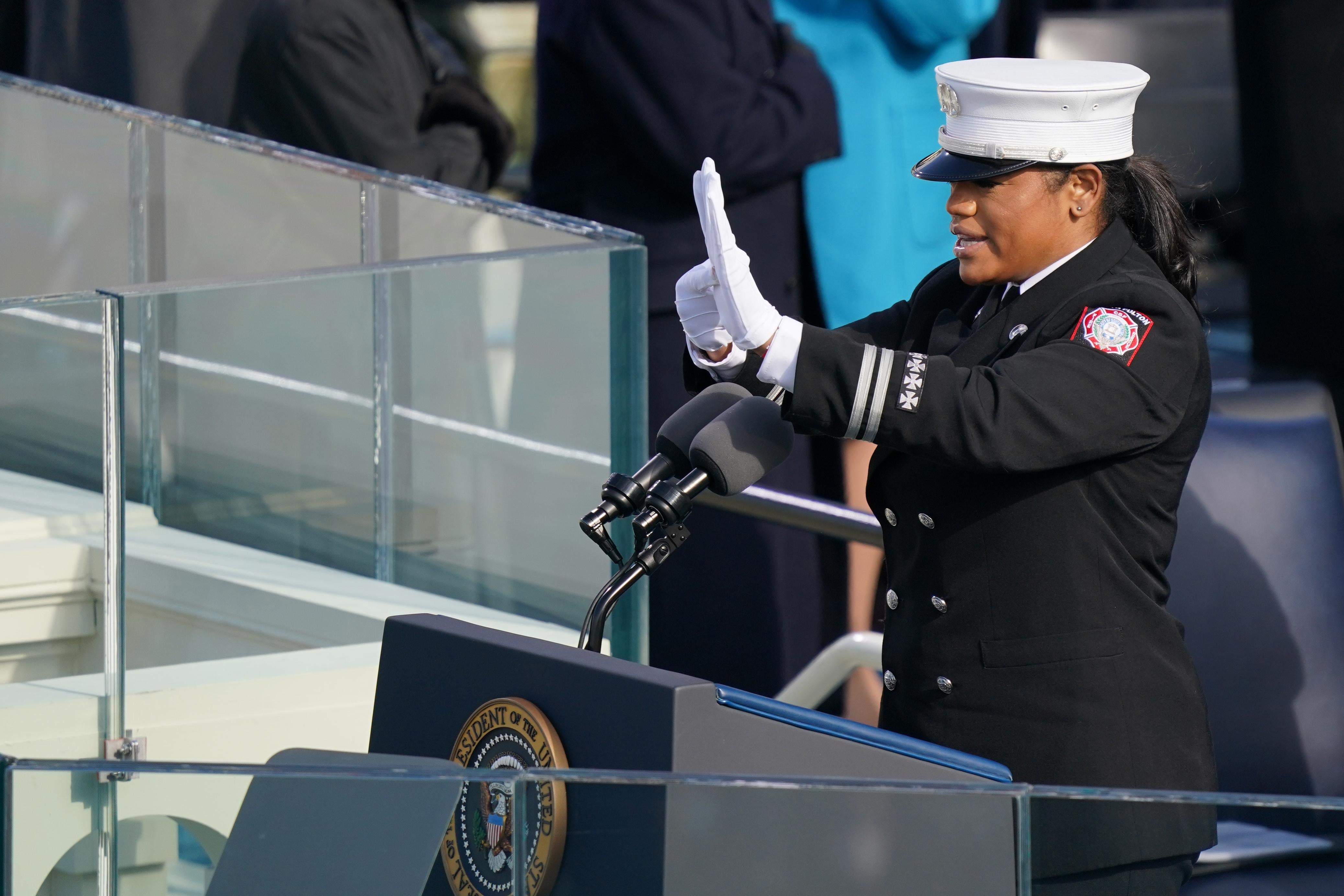 A woman in uniform at a lectern signs.