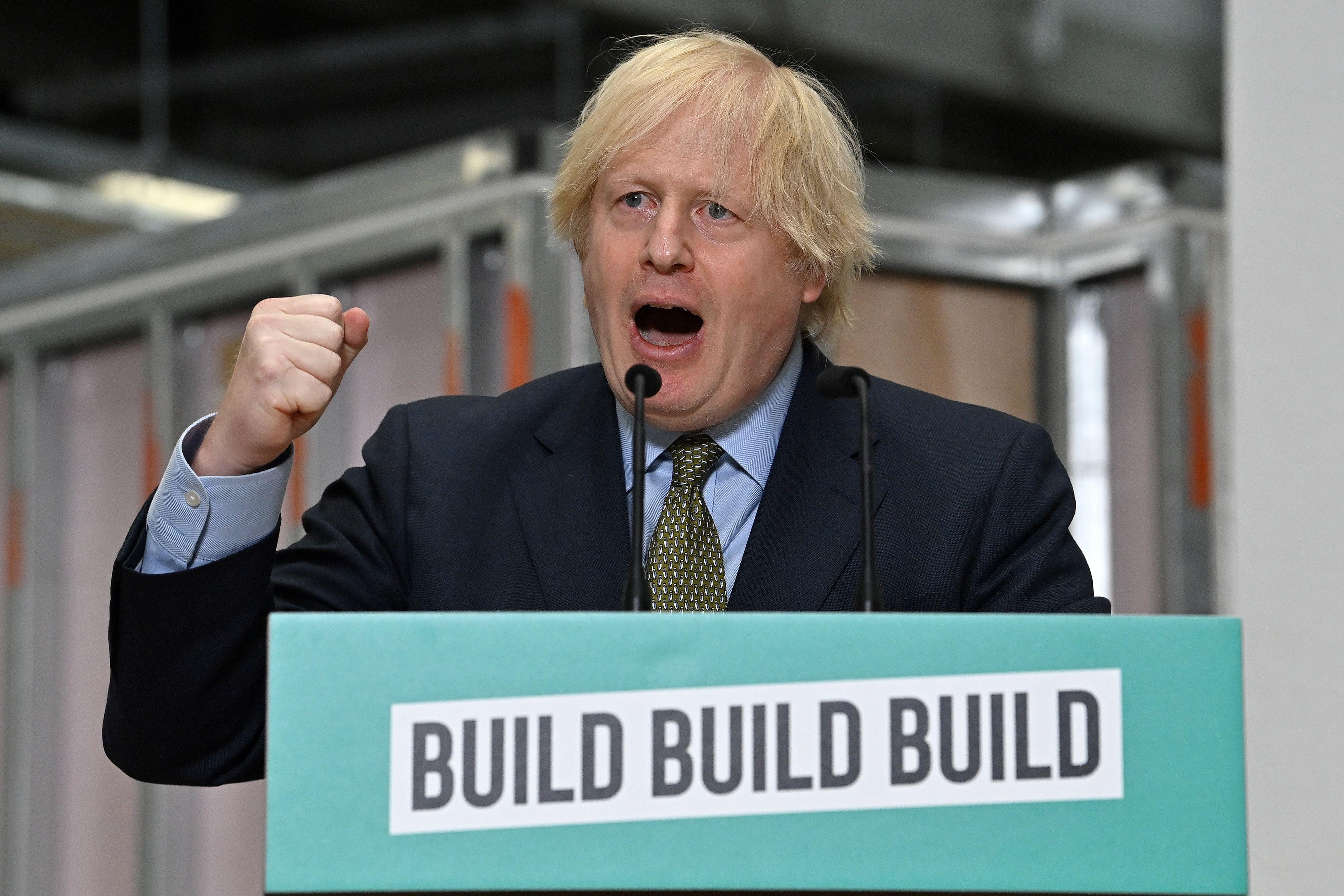 Boris Johnson raises his fist while speaking at a lectern with a sign that reads "Build, Build, Build."