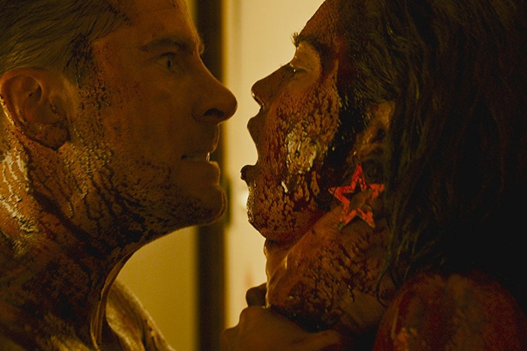 Kevin Janssens and Matilda Lutz in Revenge. Janssens grips Lutz by the throat and stares at her. They are both covered in blood.