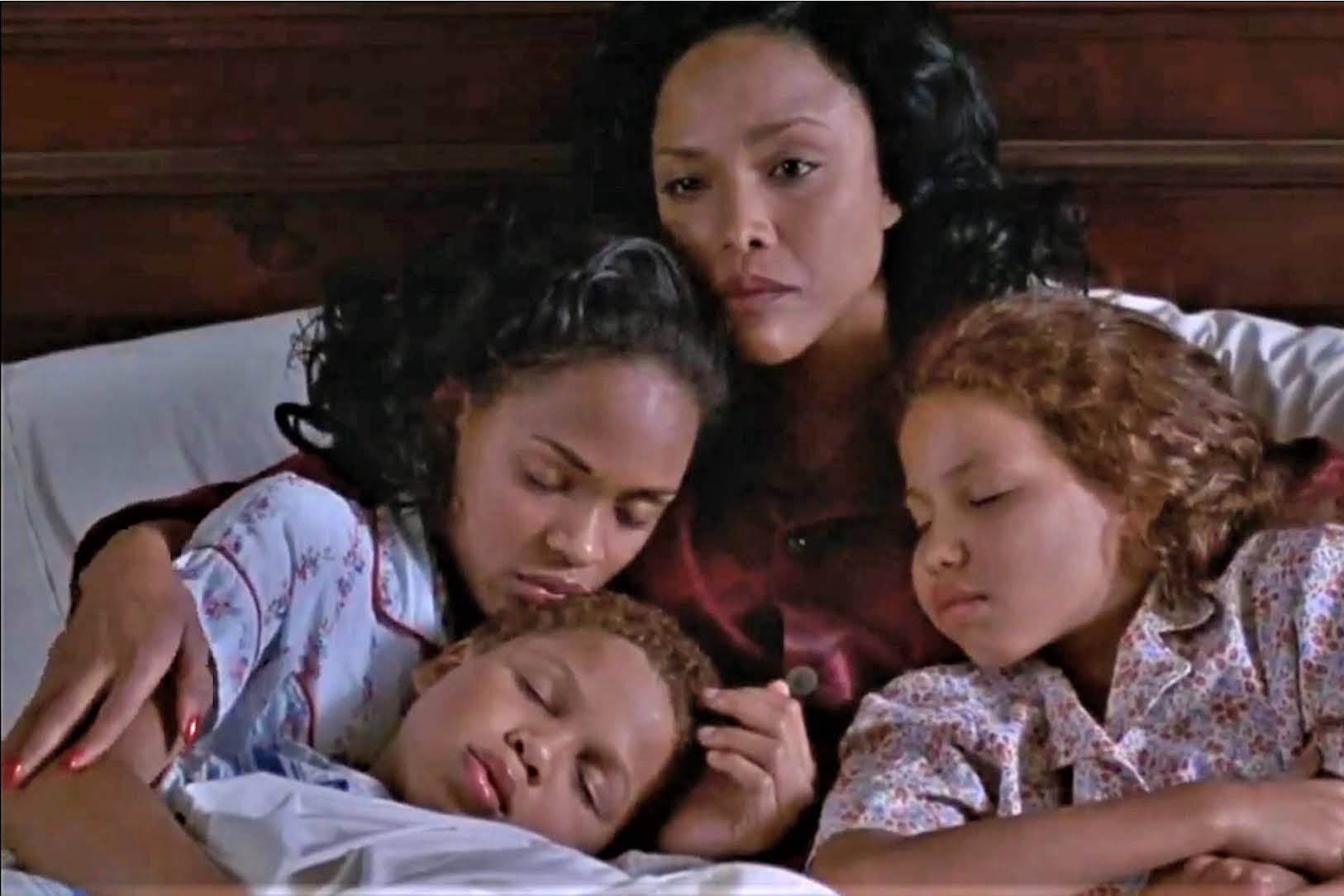 A mother holds her three children in her arms as they lie in bed.