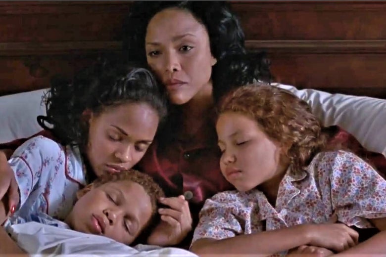 A mother holds her three children in her arms as they lie in bed.
