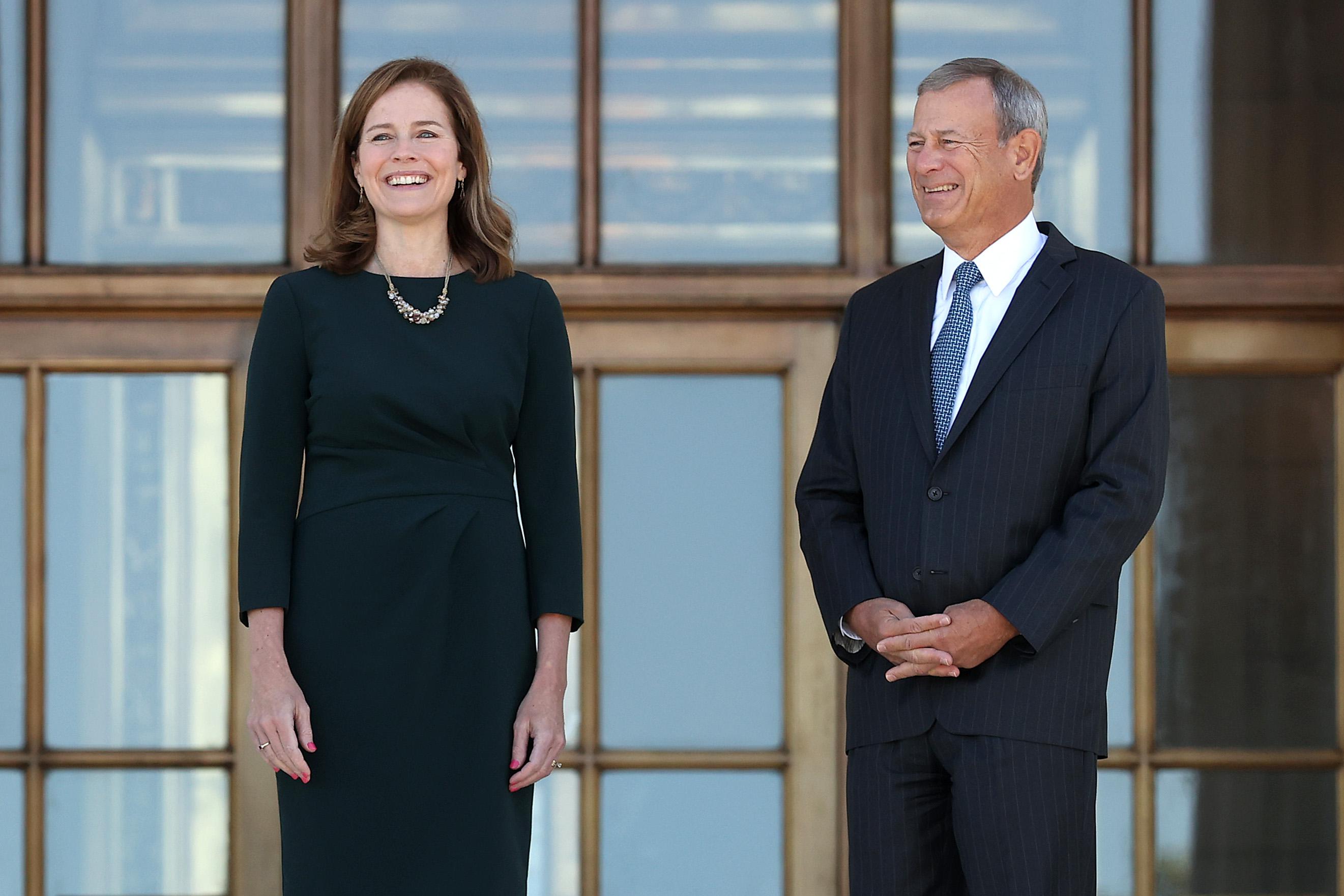Amy Coney Barrett and John Roberts stand outside and smile.