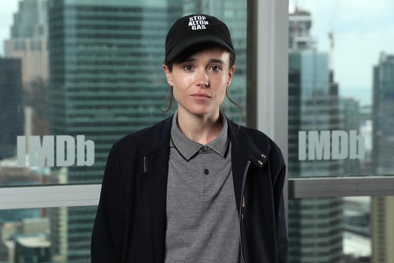Elliot Page stands in front of a window overlooking the Toronto skyline.