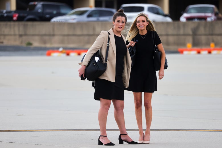 Two women in black dresses stand close to each other on the tarmac