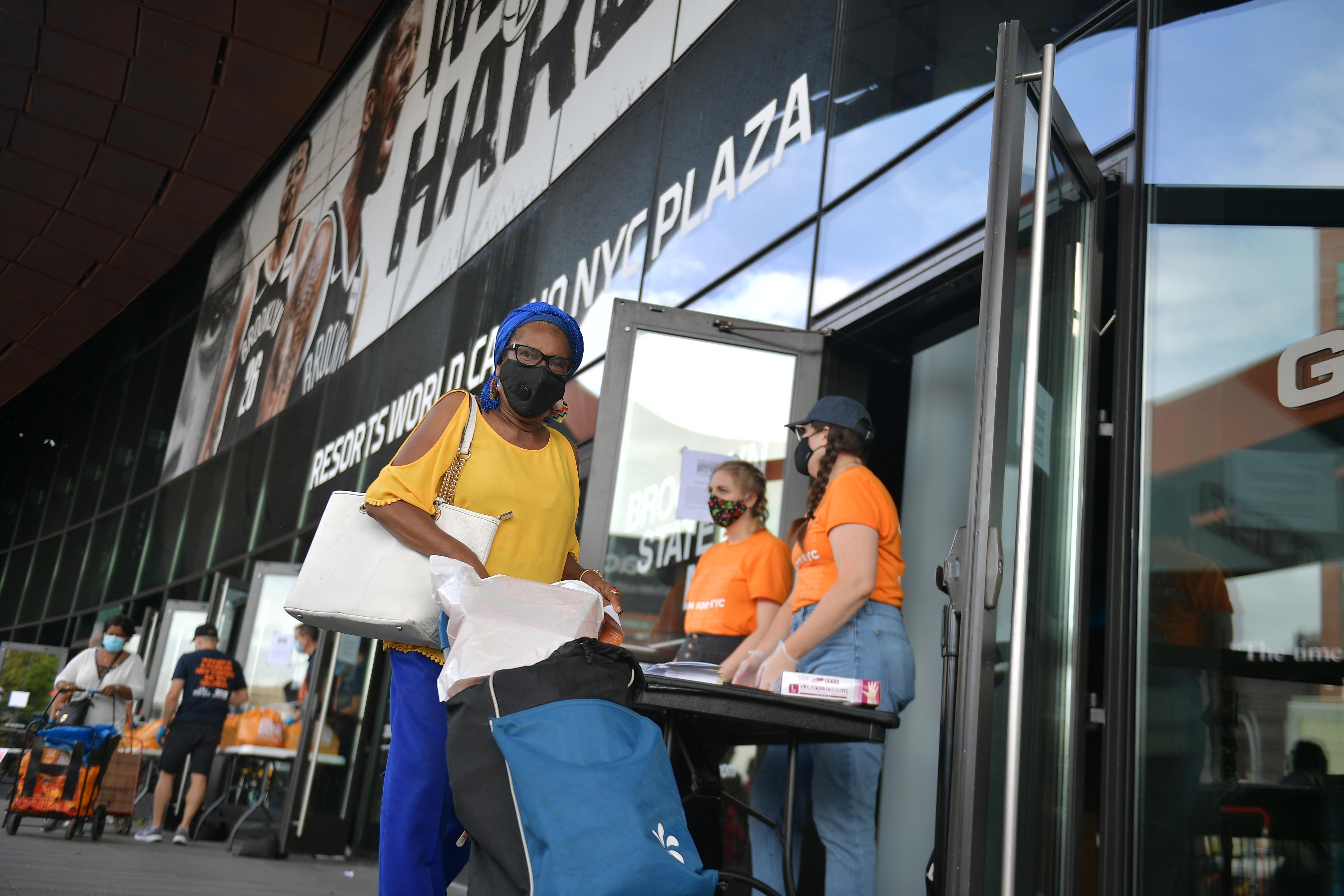 A woman pushes a rolling card with produce away from a line of folding tables set up in front of the Barclays Center.