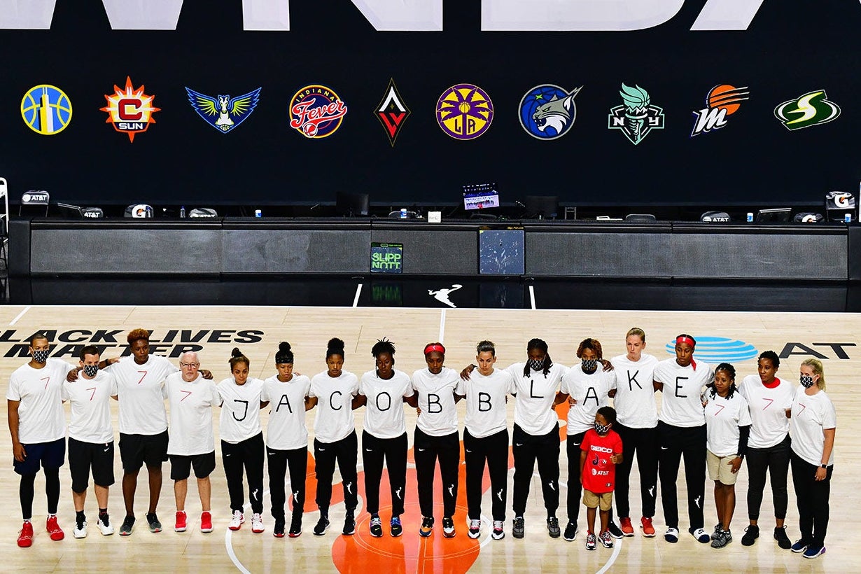 Mystics players stand in a row wearing shirts that spell out Jacob Blake's name, flanked by people in shirts that read "7."