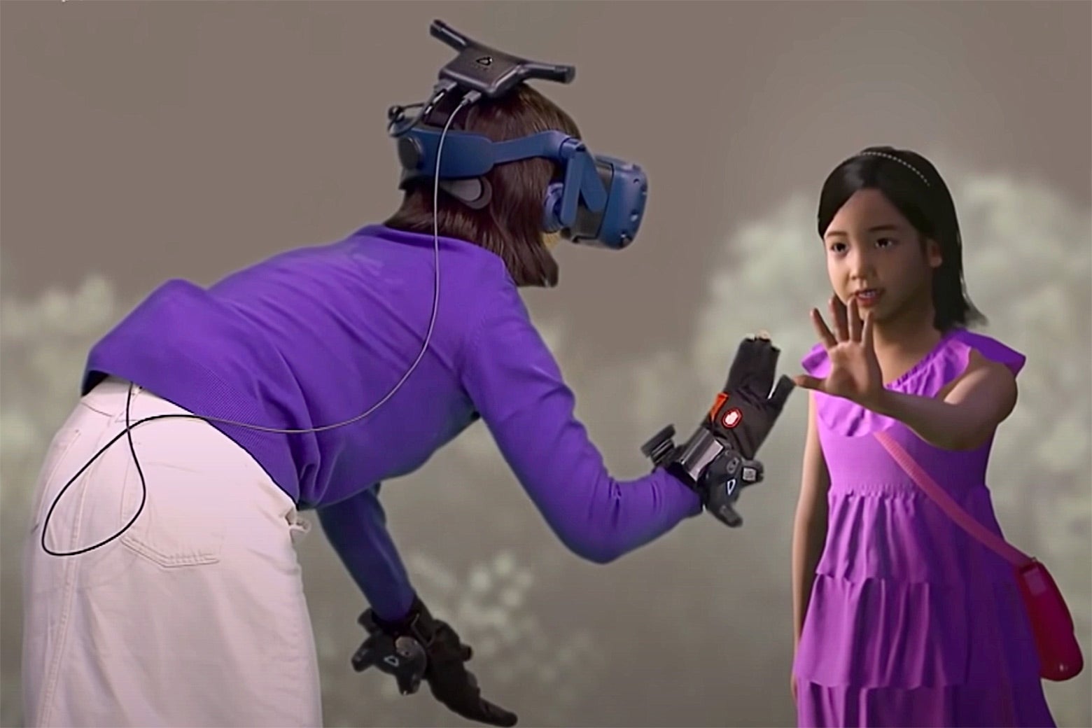 A woman in a headset and gloves reaches out to touch the hand of a young girl.