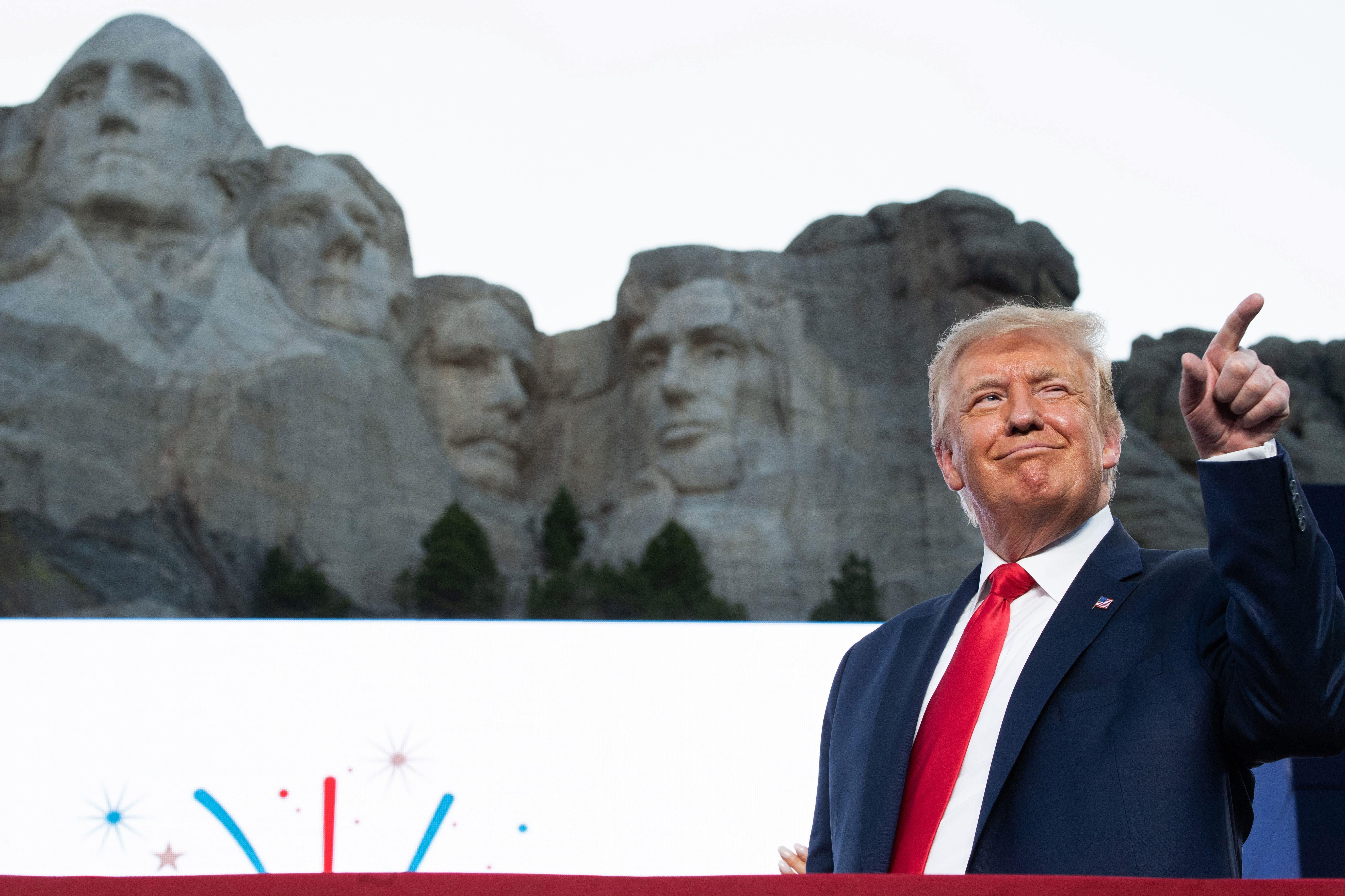 Donald Trump points and smiles while standing in front of Mount Rushmore.