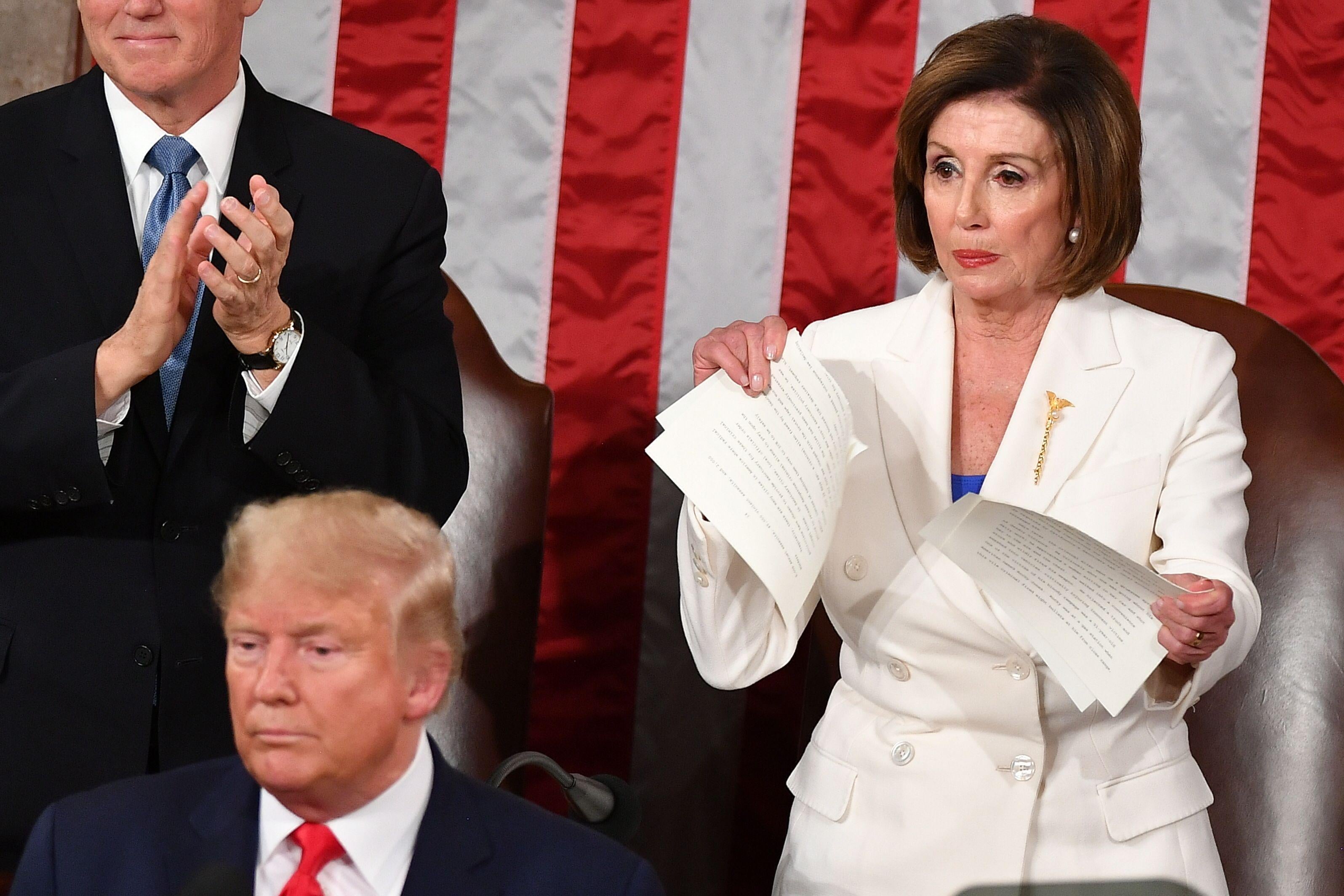 Nancy Pelosi, standing behind Donald Trump, rips apart some sheets of paper.