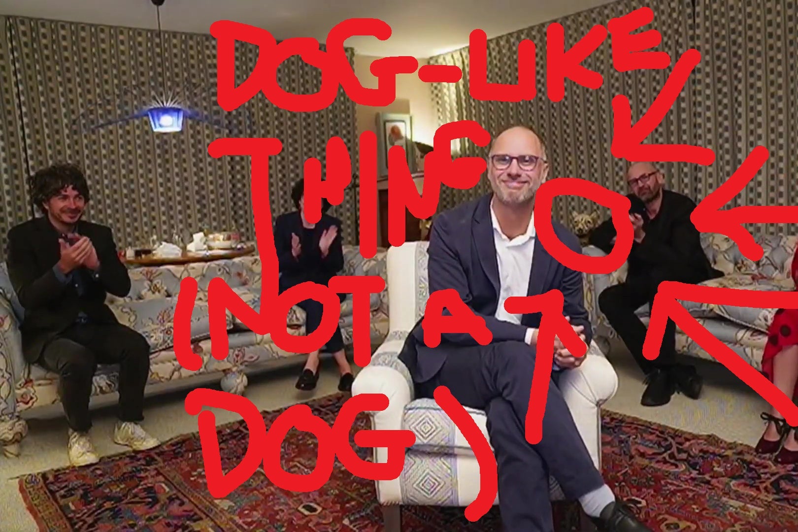 The same shot of Jesse Armstrong in a living room, but the head of a dog sculpture behind one of the couches has been pointed out with bright red arrows.