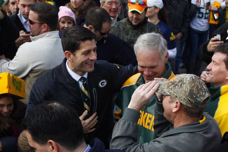 Ryan, wearing a coat with a Green Bay Packers logo on it, stands in a crowd of people wearing Packers colors, one of whom is wearing a large "cheesehead" hat.