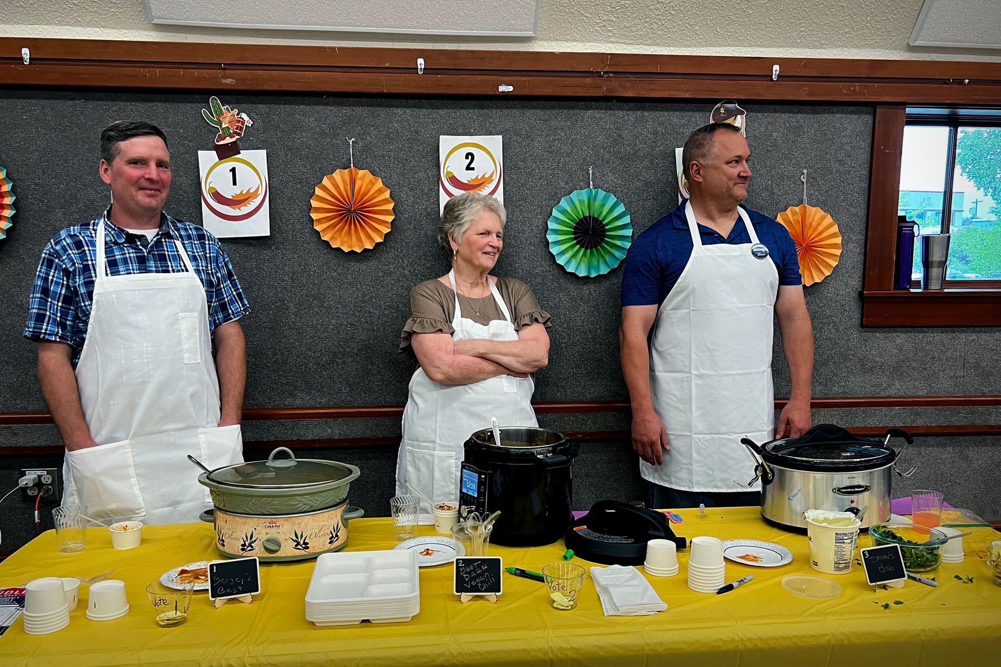 Three chefs stand behind slow cookers featuring their chili.