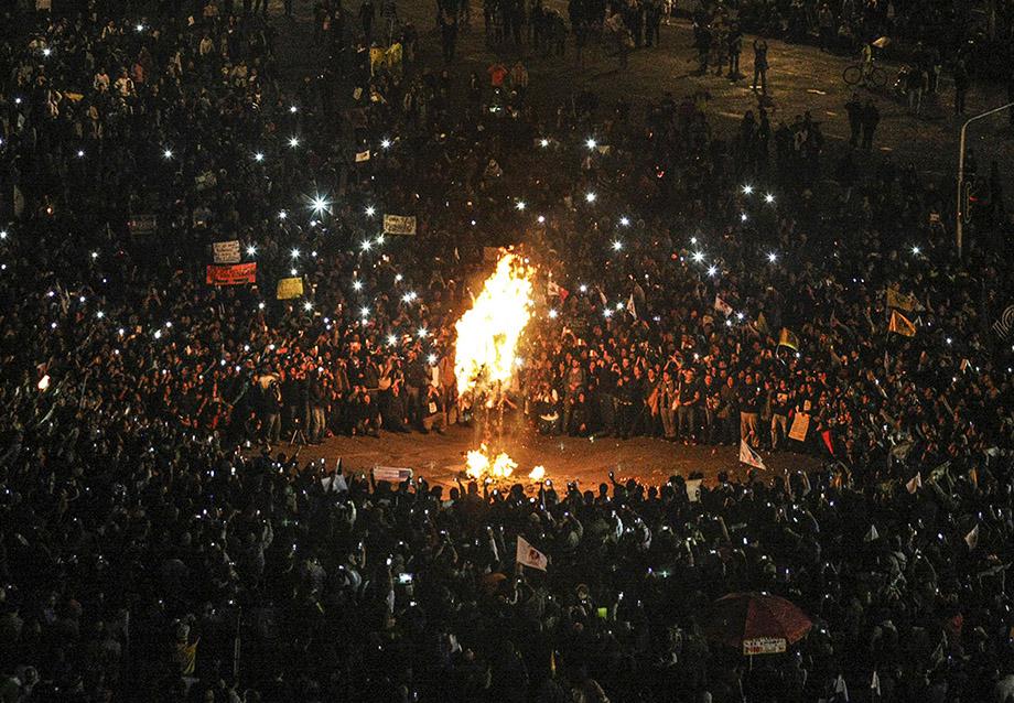 Demonstrators look at a burning effigy of President Enrique Pena