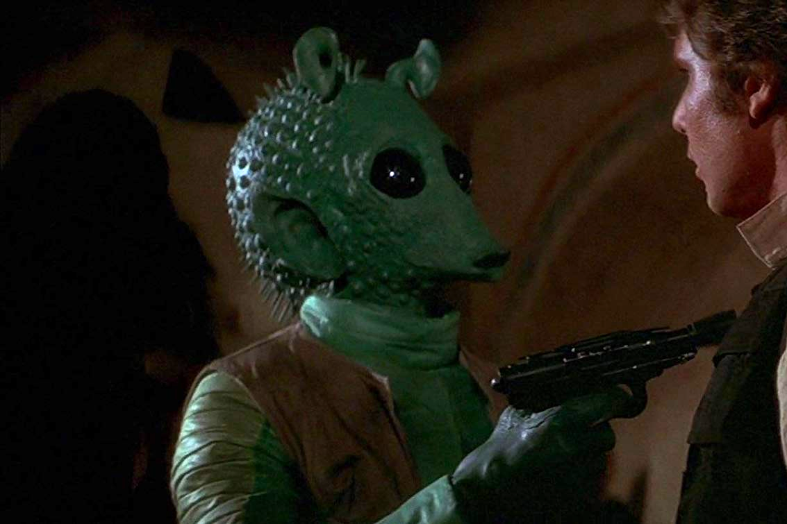 Greedo, a green alien, points a blaster at Han Solo.