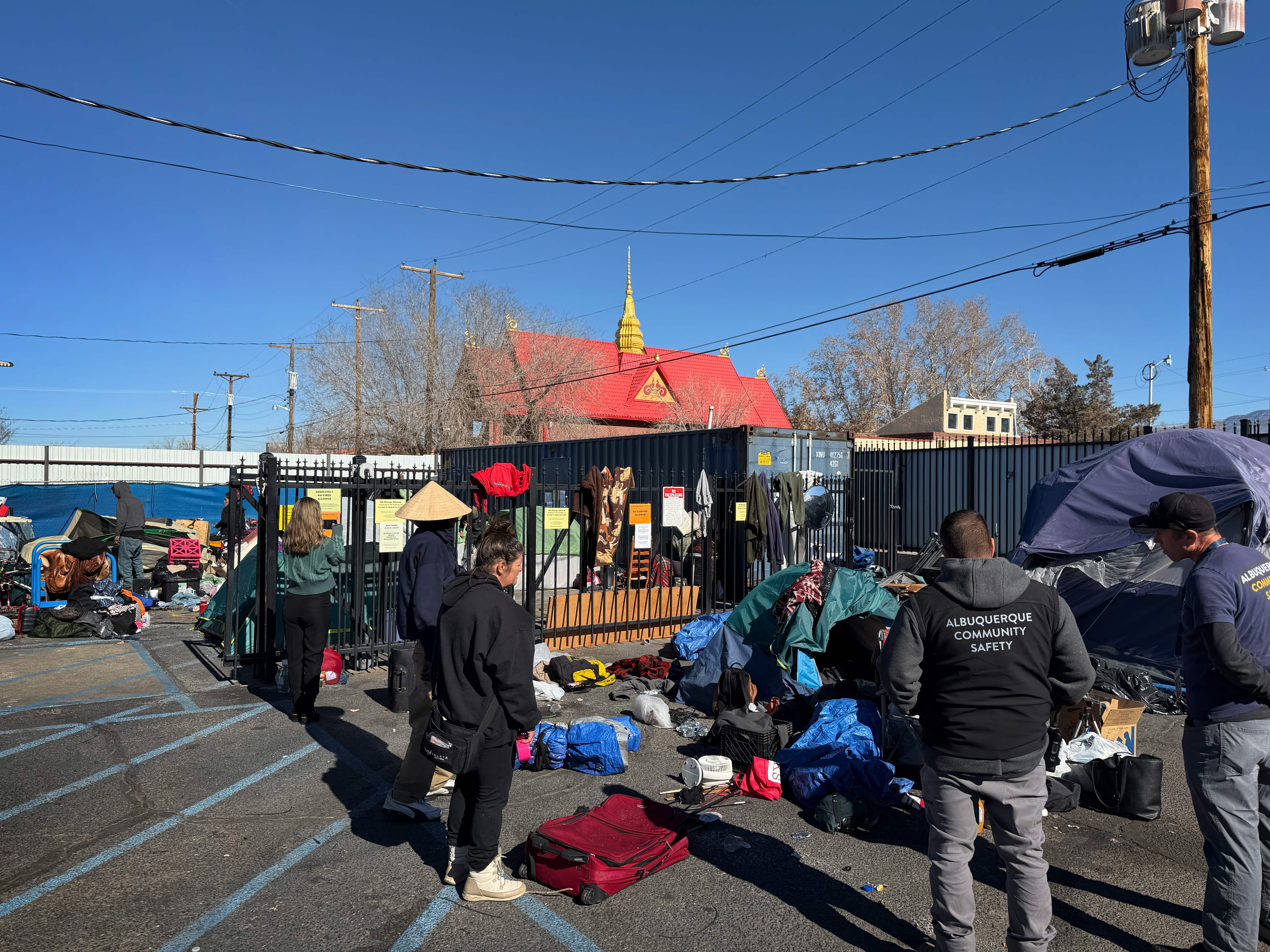 Two people wearing Albuquerque Community Safety jackets stand near two tents.