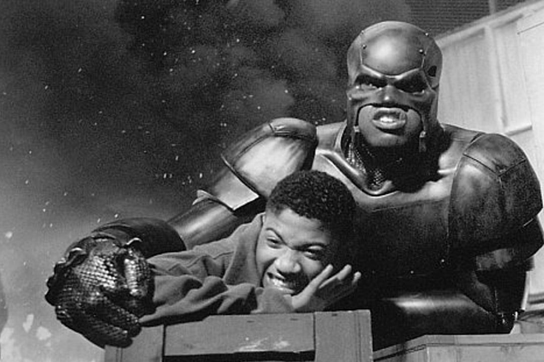 Still from the movie Steel of Shaquille O’Neal in his Steel armor saving a boy, with an explosion in the background