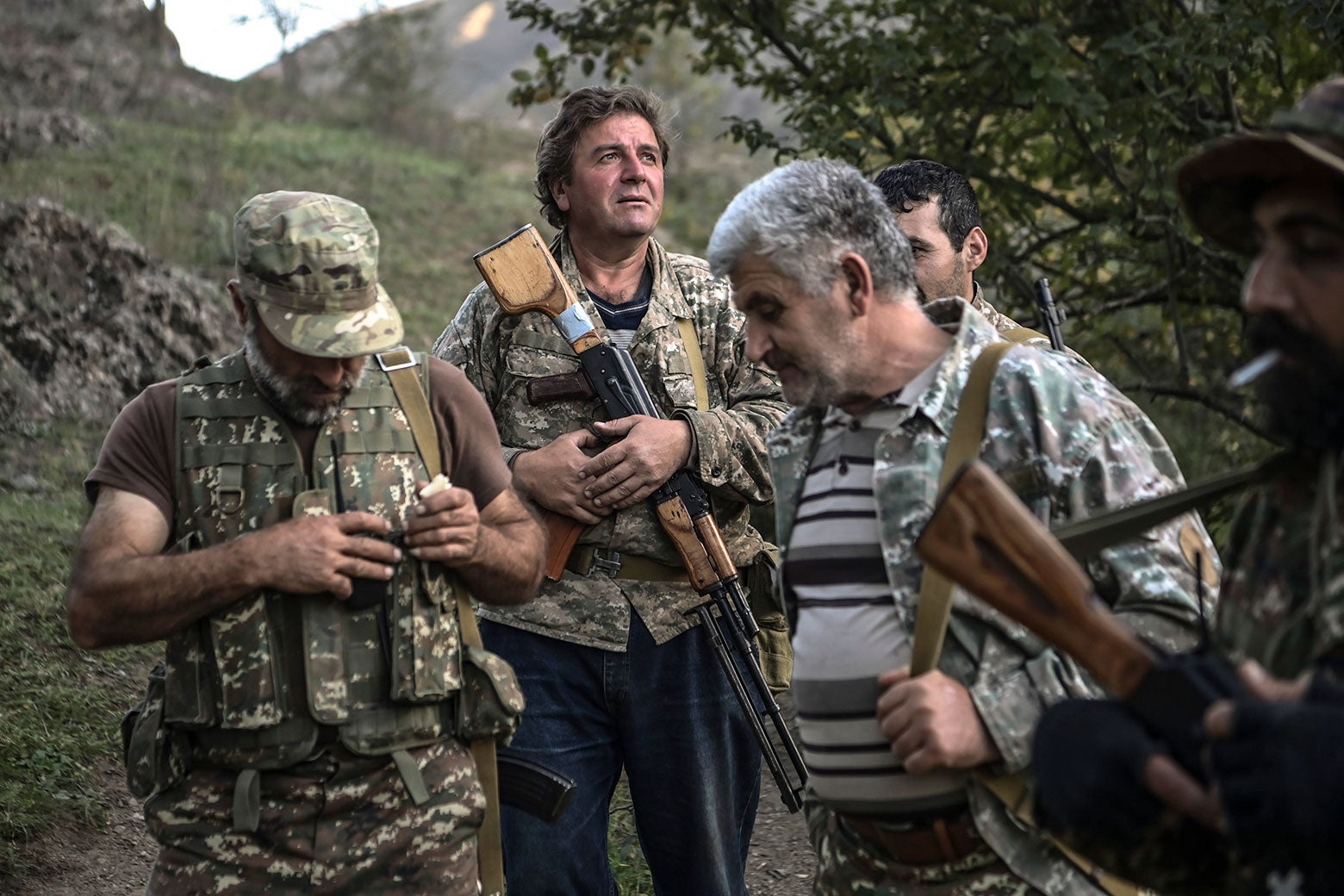 Men in camouflage stand around. One is smoking a cigarette.