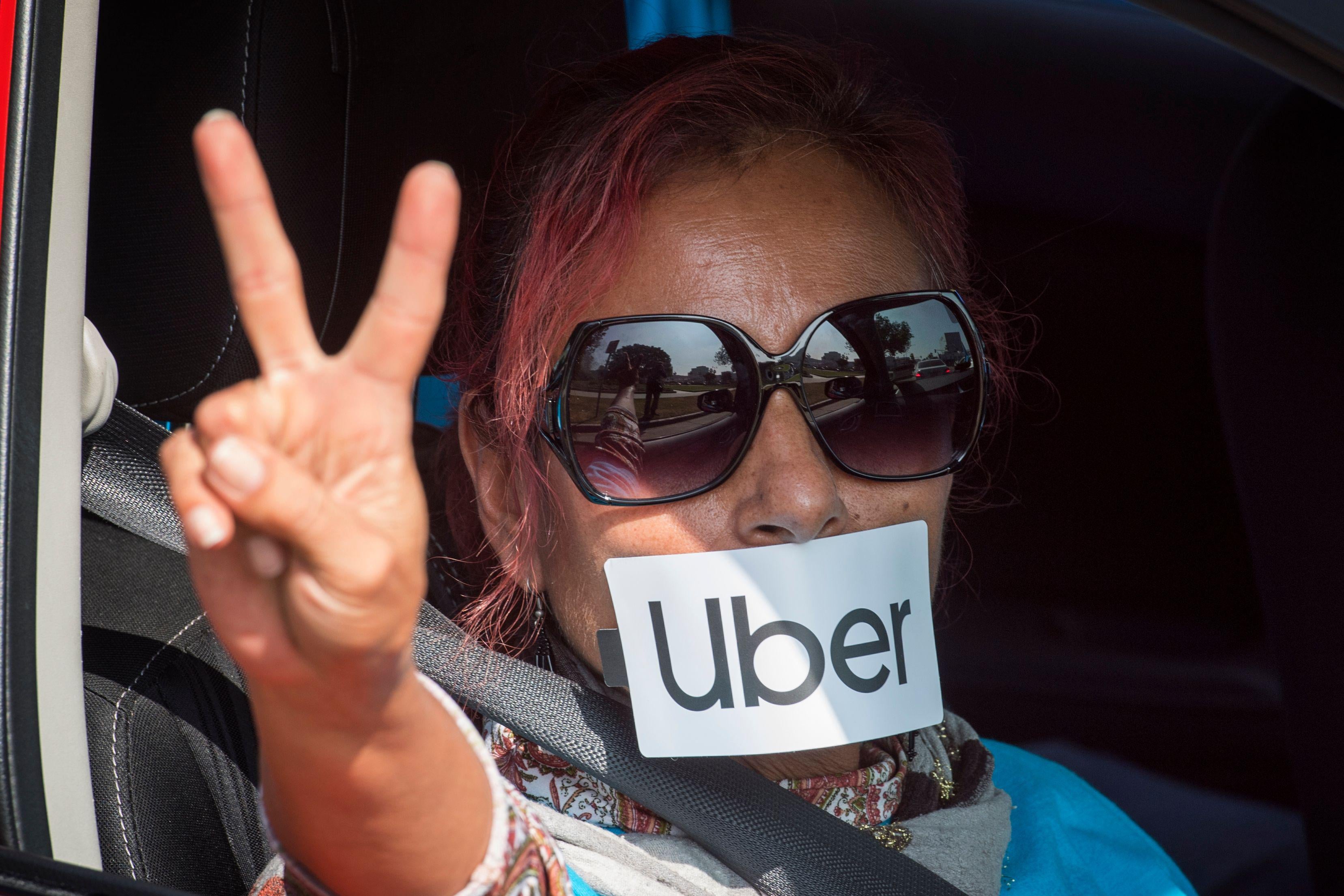 A woman sitting in a car making a peace sign with her hands with an Uber sticker on her mouth