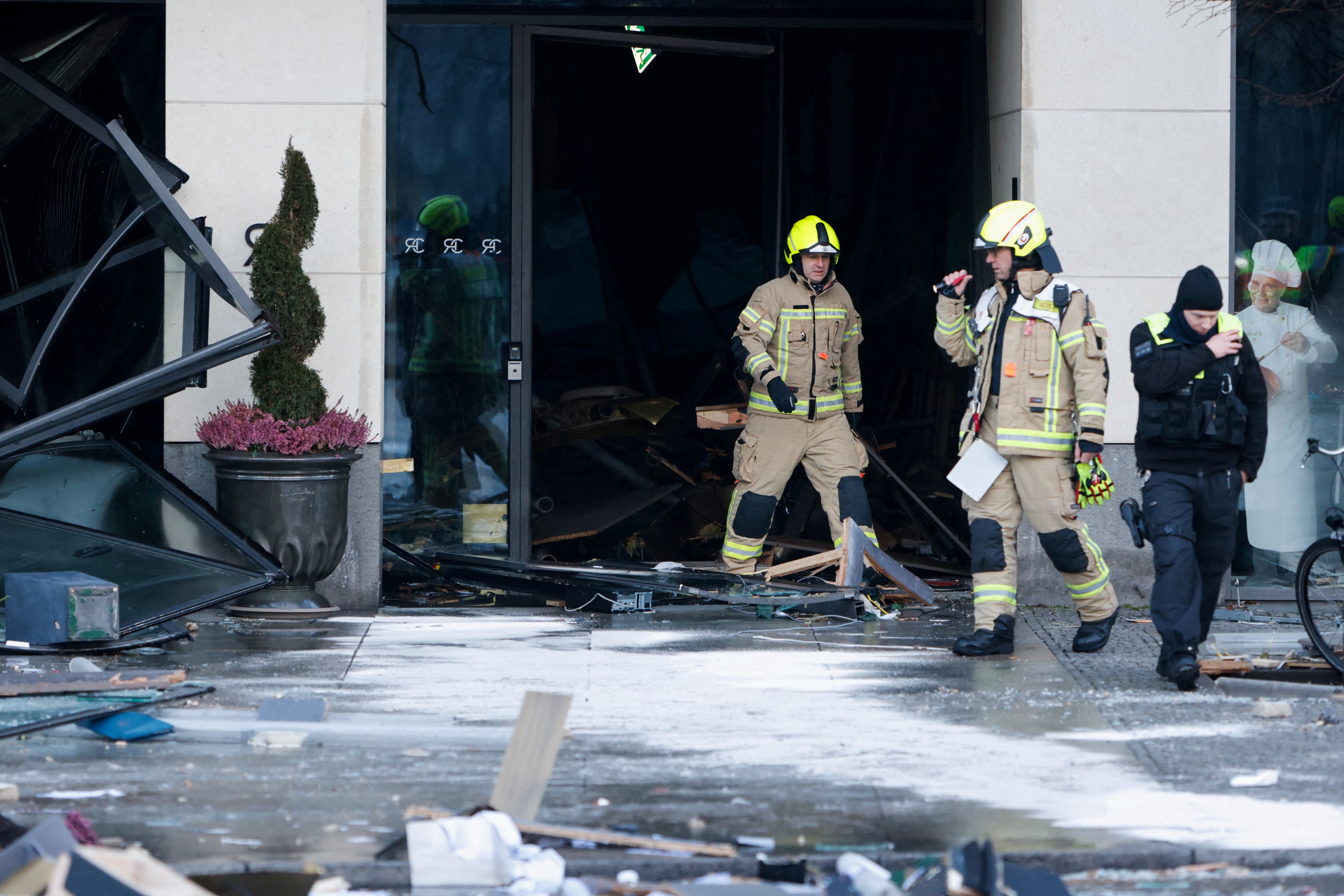 Emergency workers outside of a building, with a lot of broken glass and debris around them.