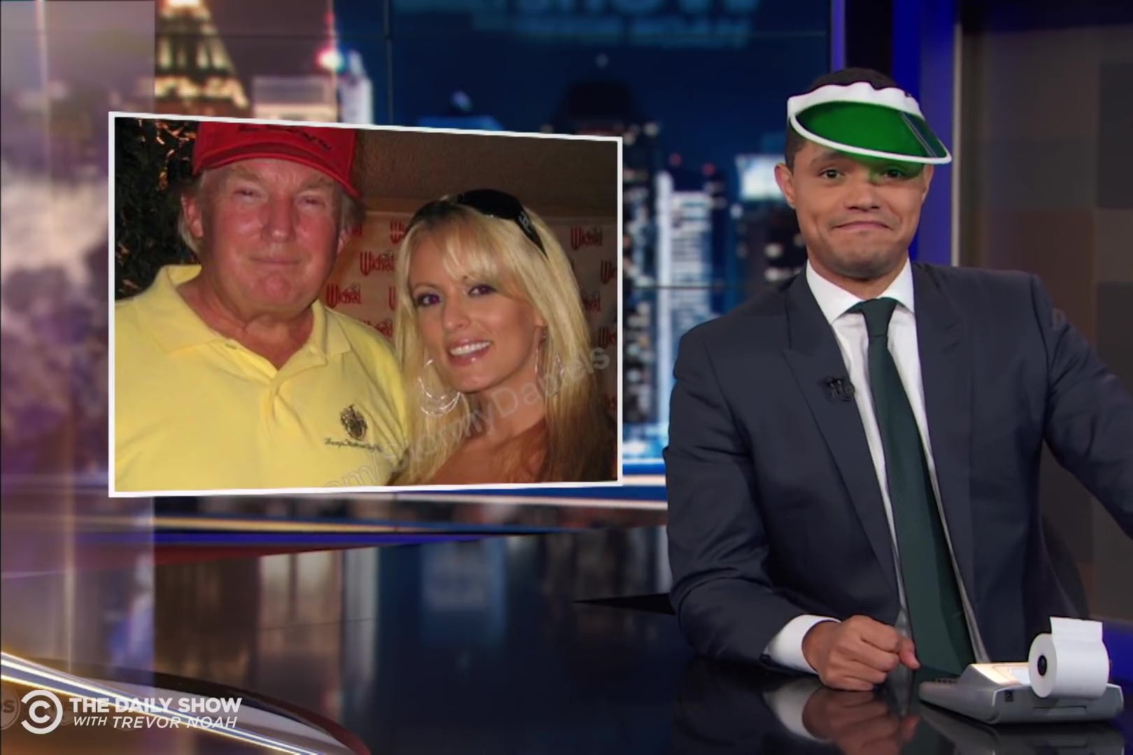 Trevor Noah, wearing an accountant's green eyeshade, in front of a picture of Trump and Stormy Daniels.