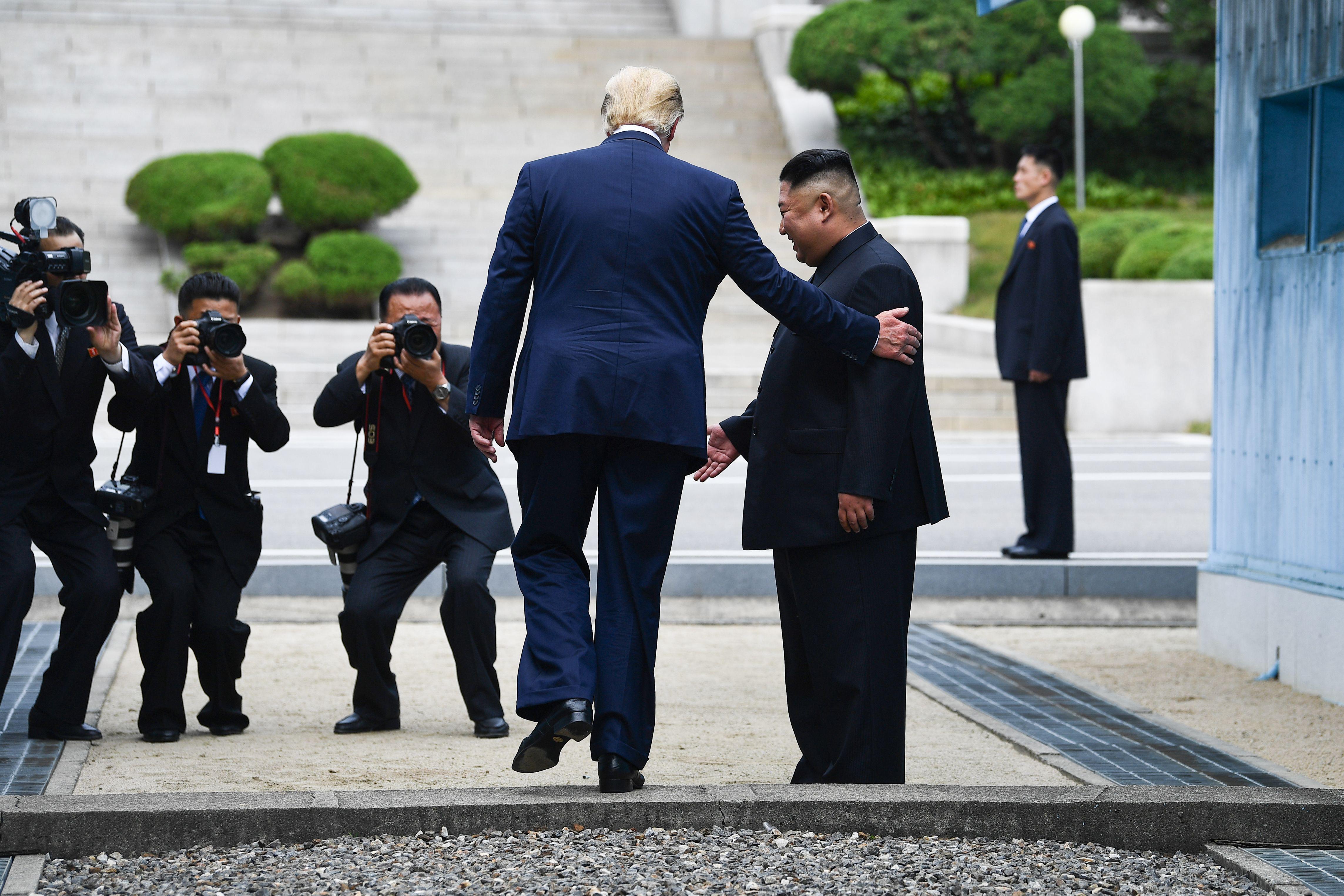 Trump walks across the border as Kim looks on.
