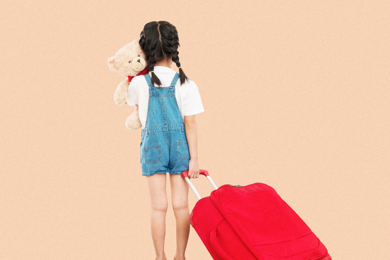 A child with braids hugs a teddy bear while pulling a suitcase.