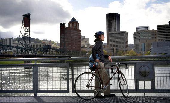 Man with bicycle looking at skyline over river, Portland, Oregon.