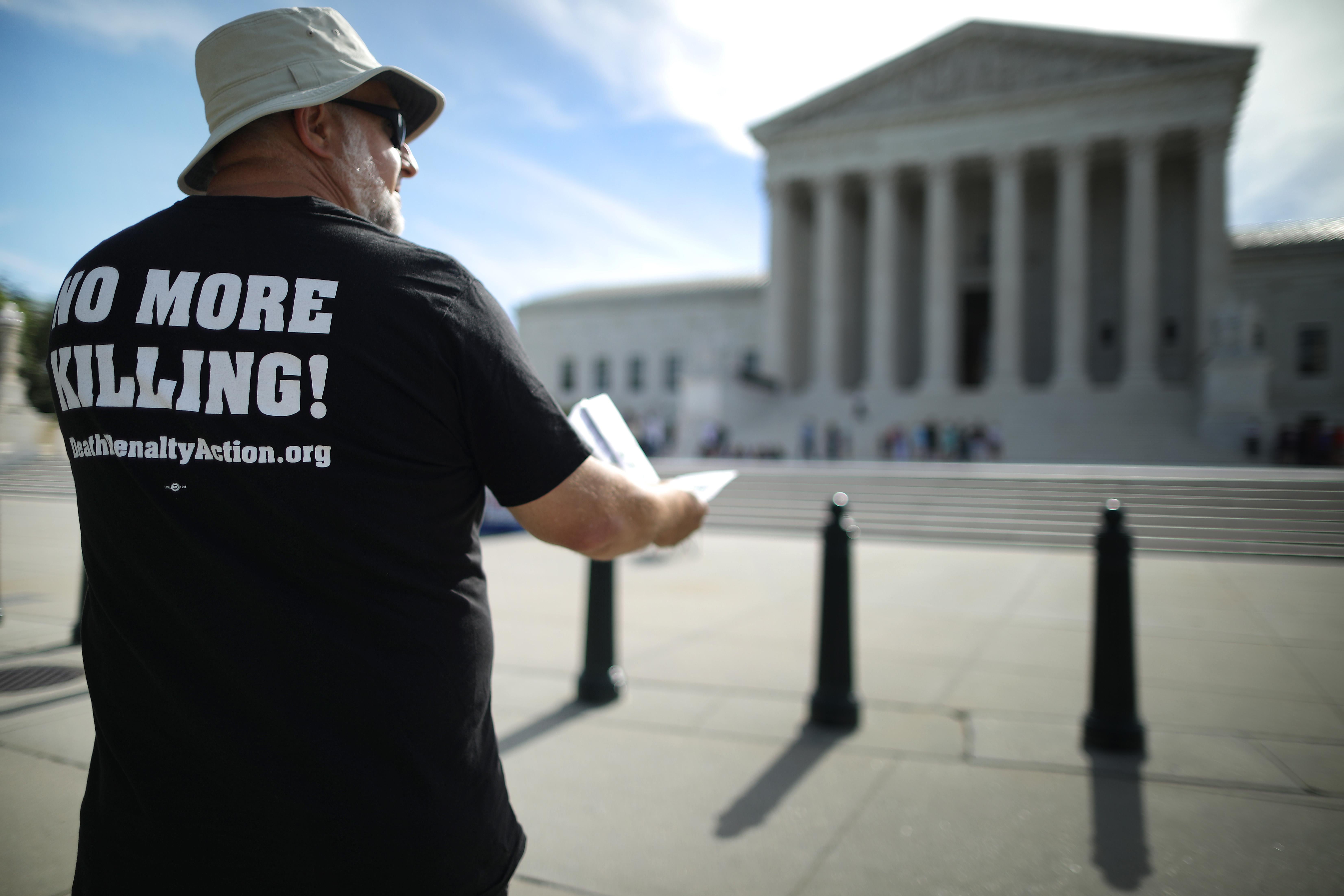 A death penalty abolitionist wearing a T-shirt that says "NO MORE KILLING" protests in front of the Supreme Court