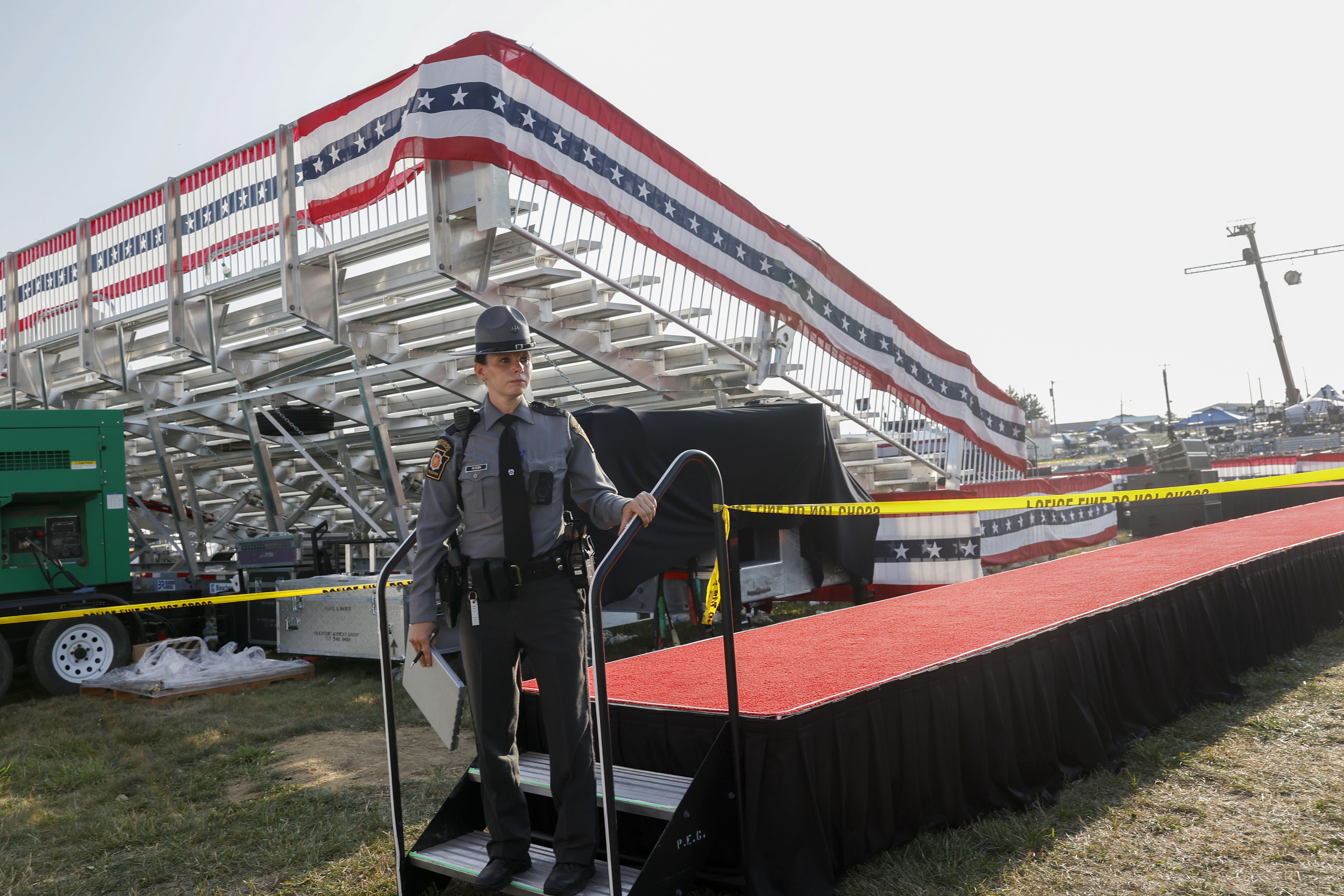 A law enforcement agent stands near the stage of the Trump campaign rally after it has been evacuated. She looks somber and everything else is empty.