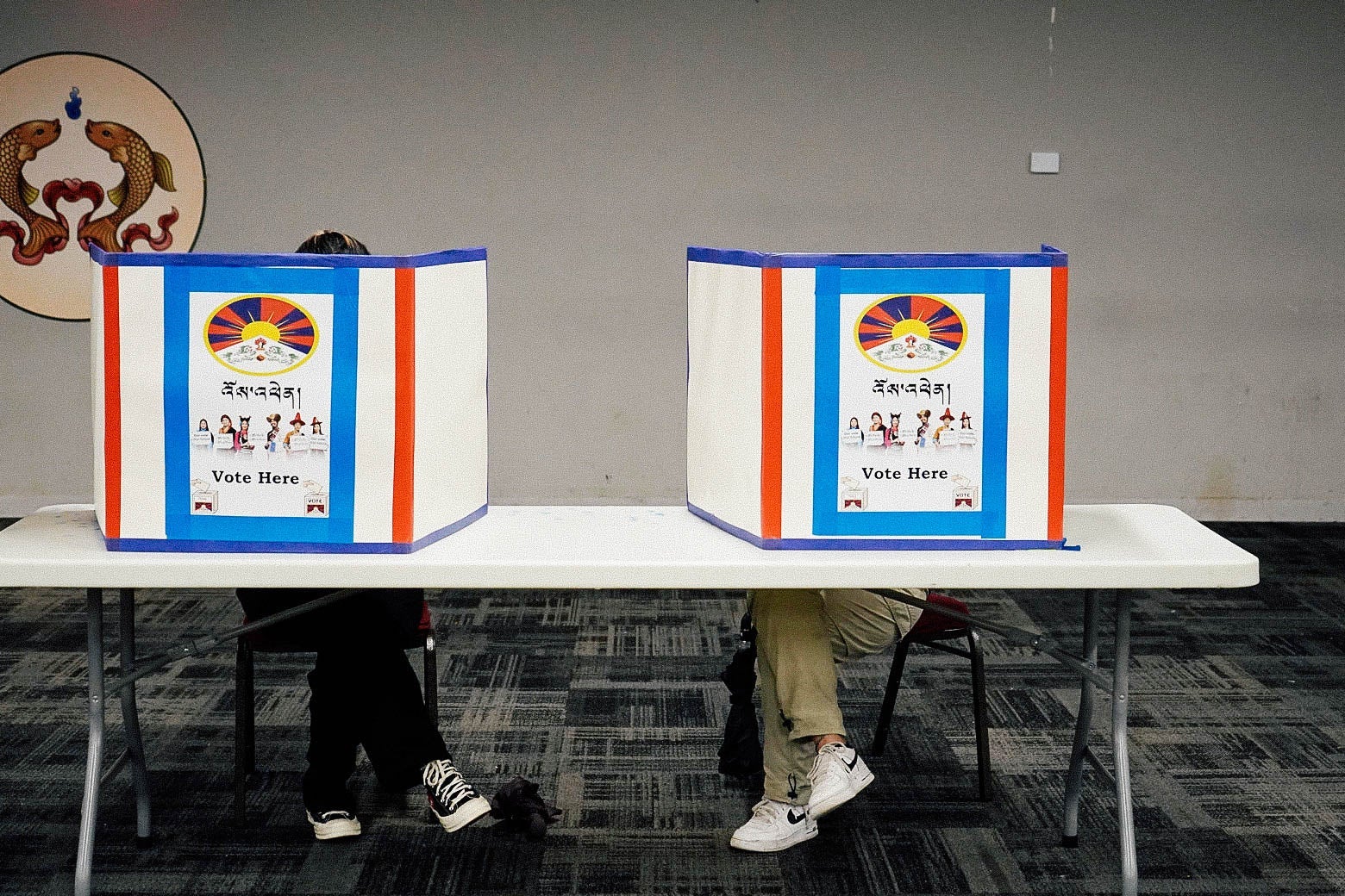Two people sit behind a folding table behind privacy booths.