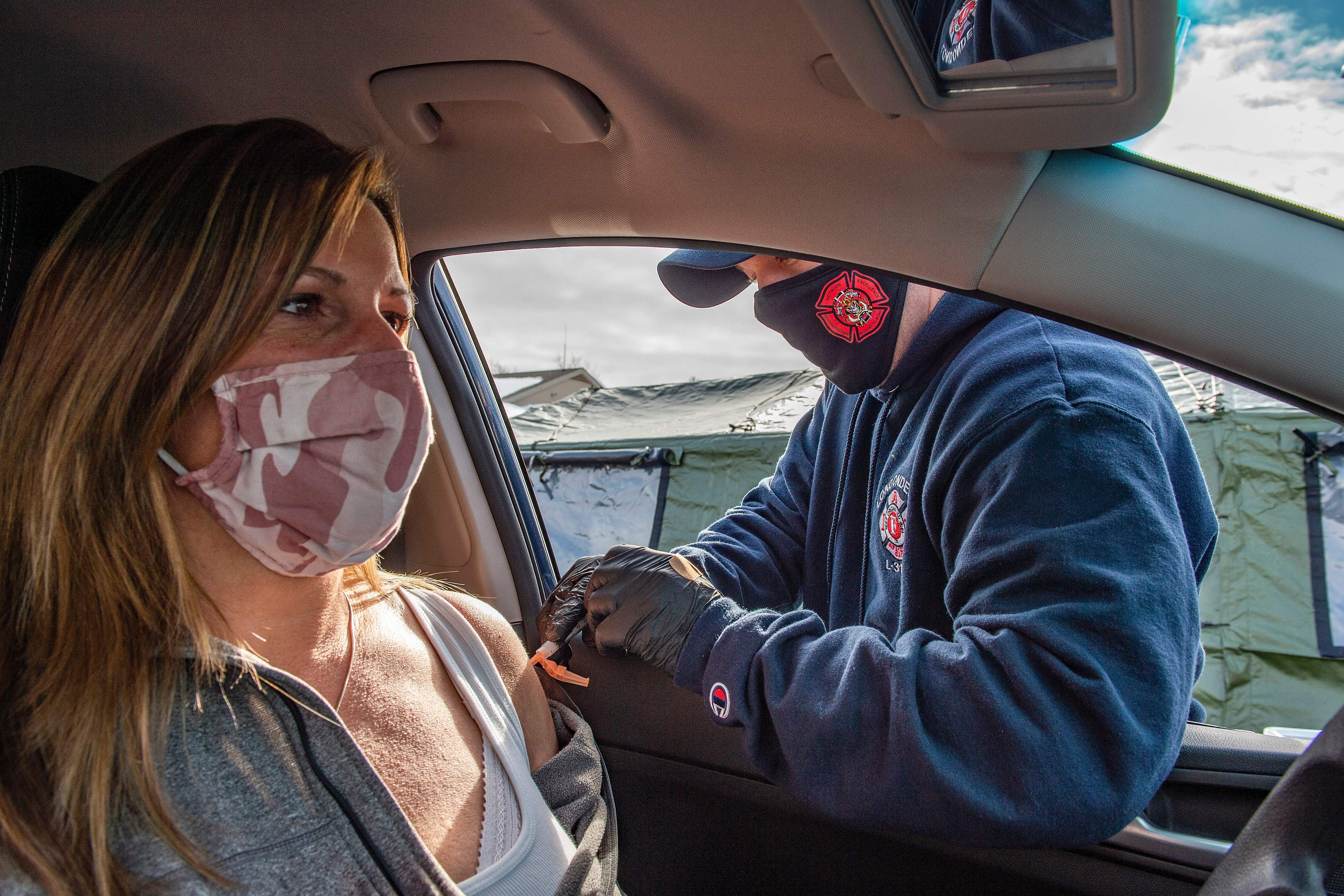A first responder vaccinates a woman through the window of her car.