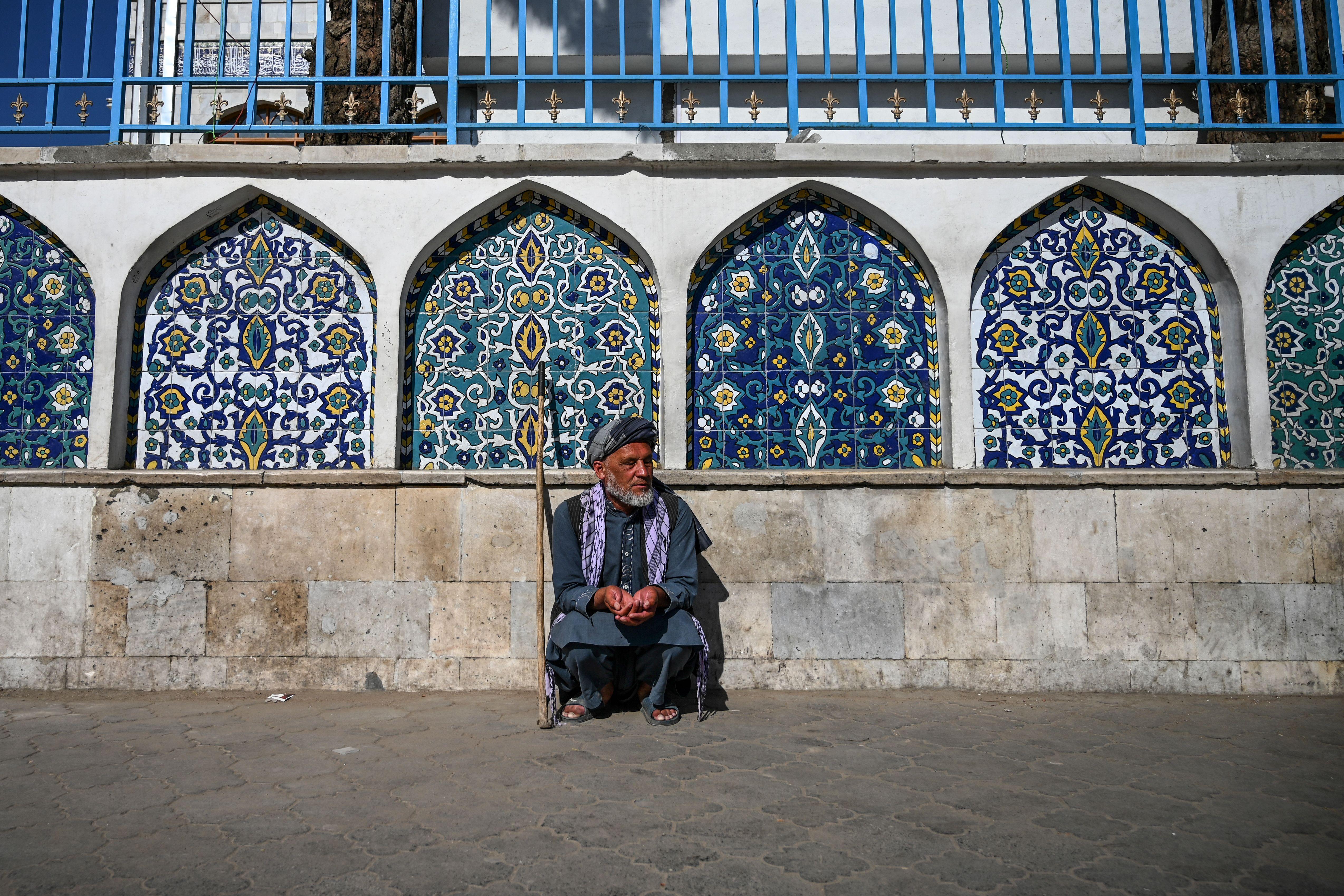 A man squats in front of ornate windows on the exterior of the mosque
