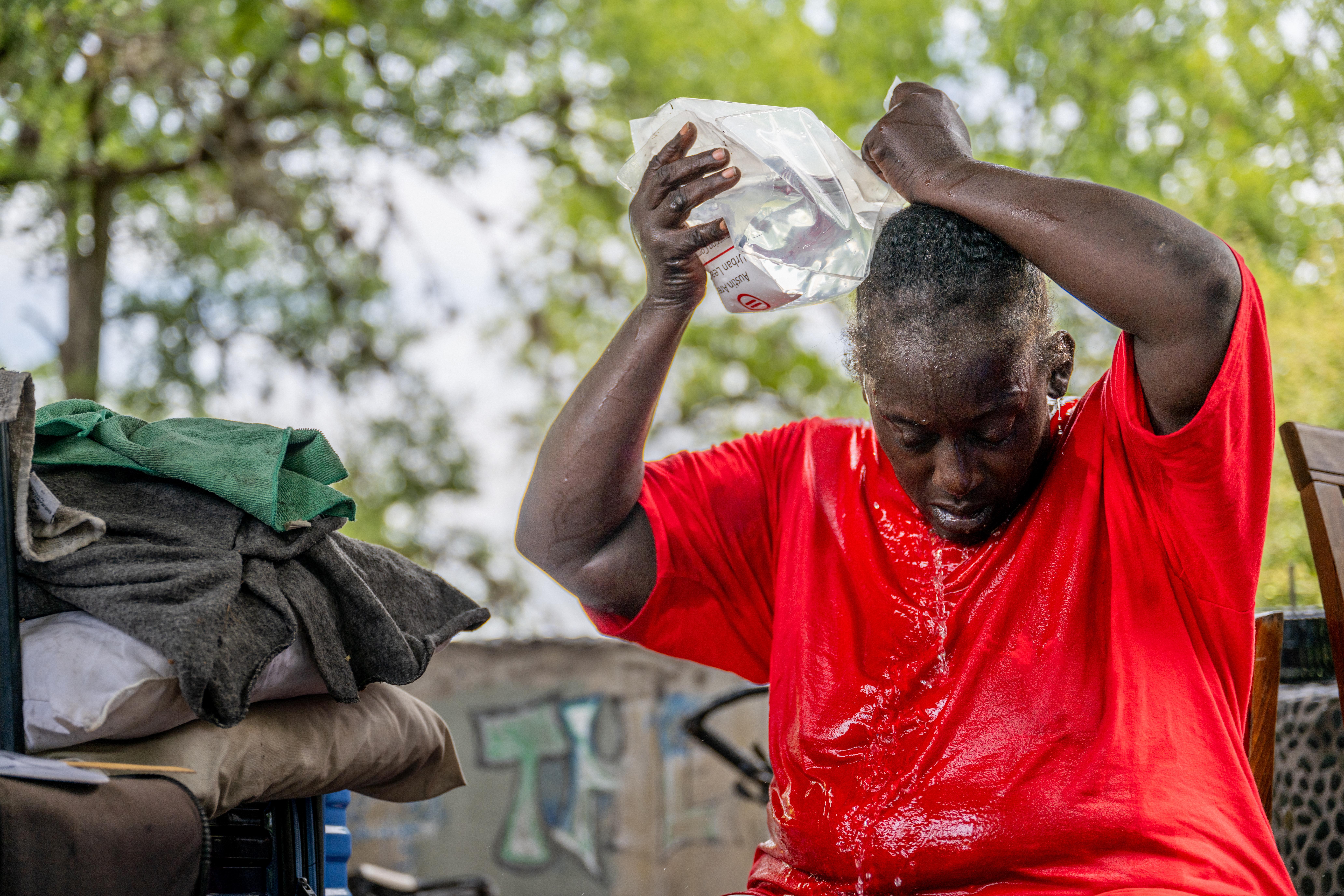 A woman in a red T-shirt sits on a bench and pours water on her head.
