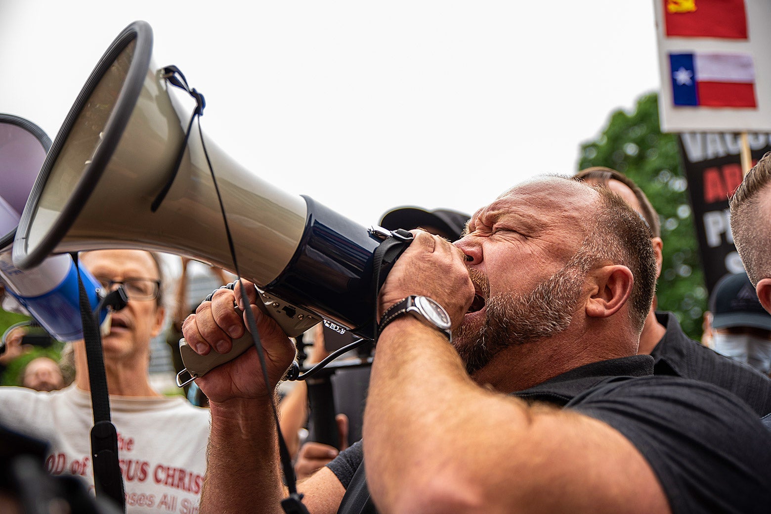 Alex Jones, in the middle of a crowd, roars into a bullhorn.
