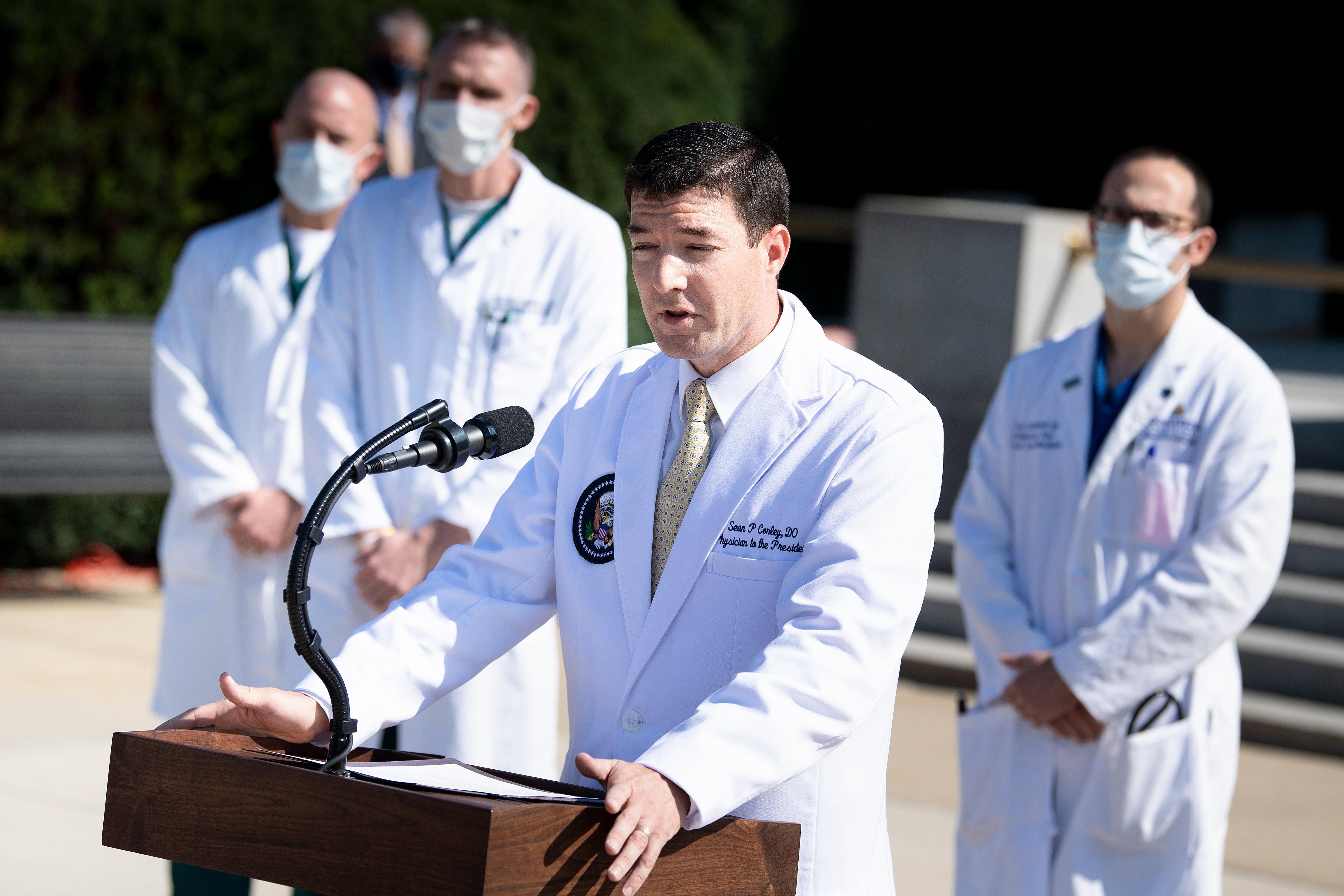 Sean Conley speaks at a lectern. Other doctors wearing masks are seen in the background.