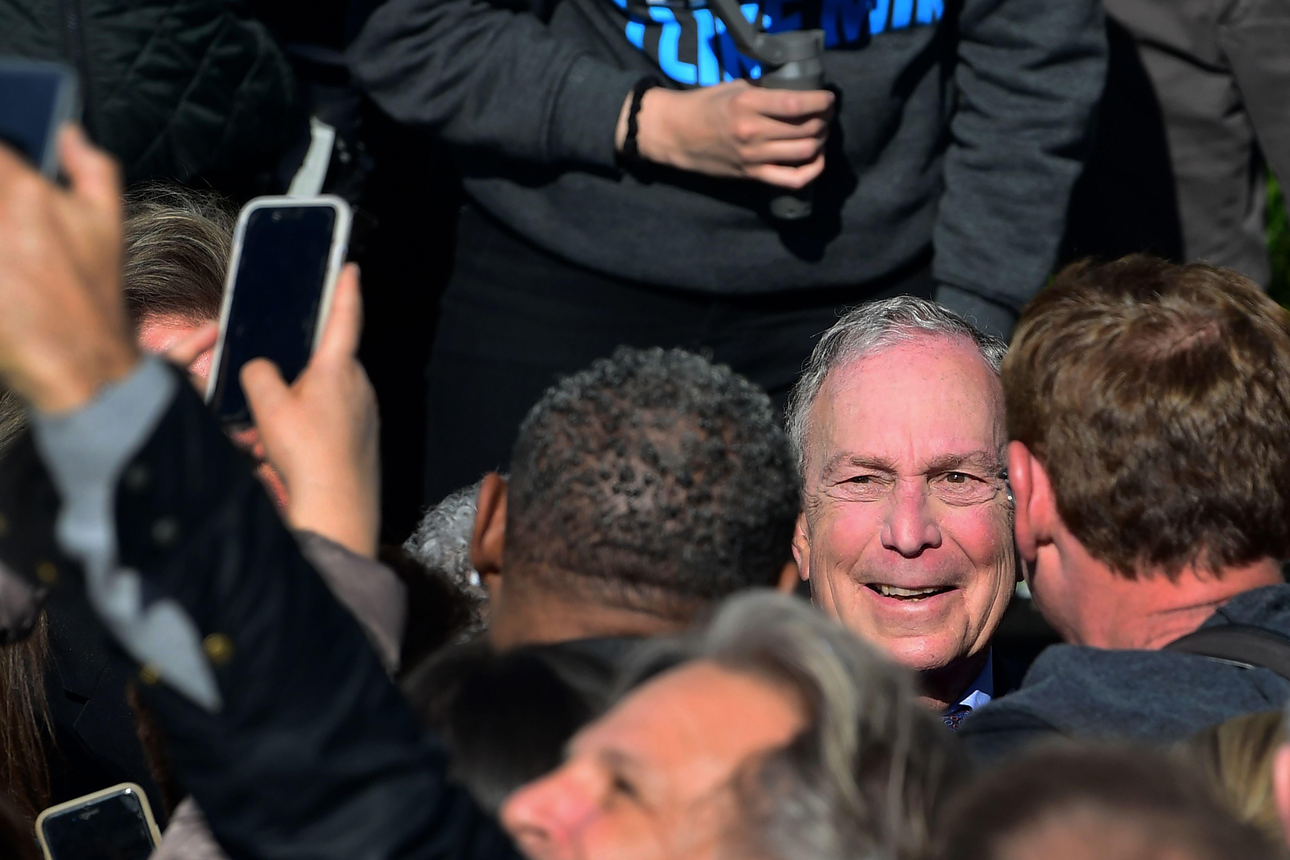 Men carrying smartphones surround Michael Bloomberg.