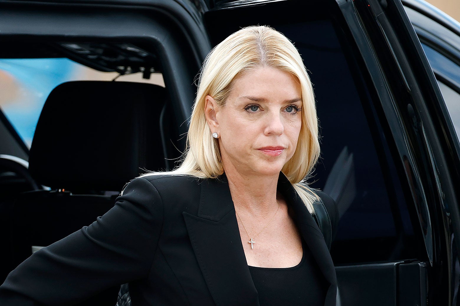 Attorney General Pam Bondi wears a cross necklace and is getting out of a car.